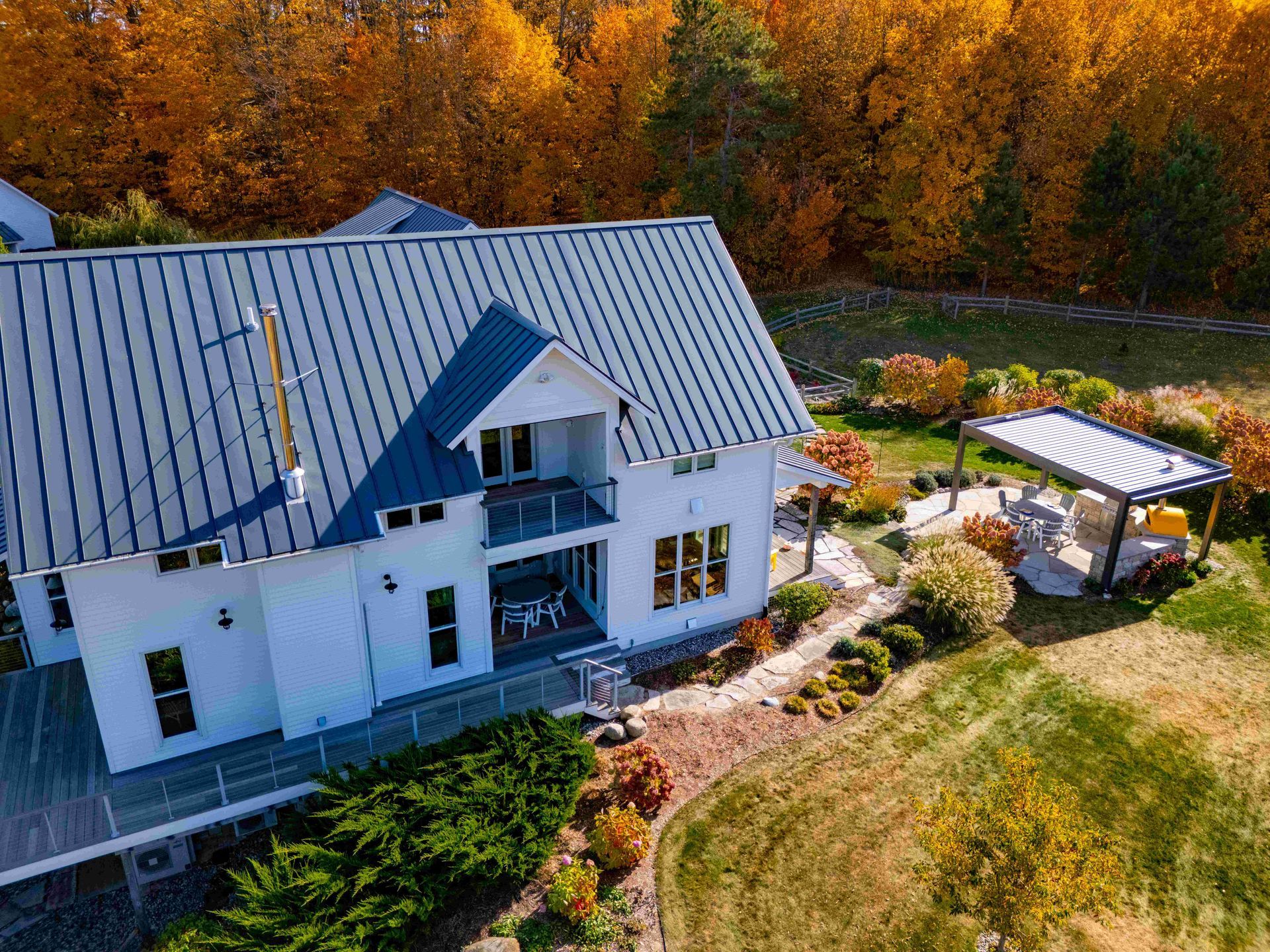 Aerial view of a white house with a blue metal roof, nestled among trees with vibrant autumn foliage.