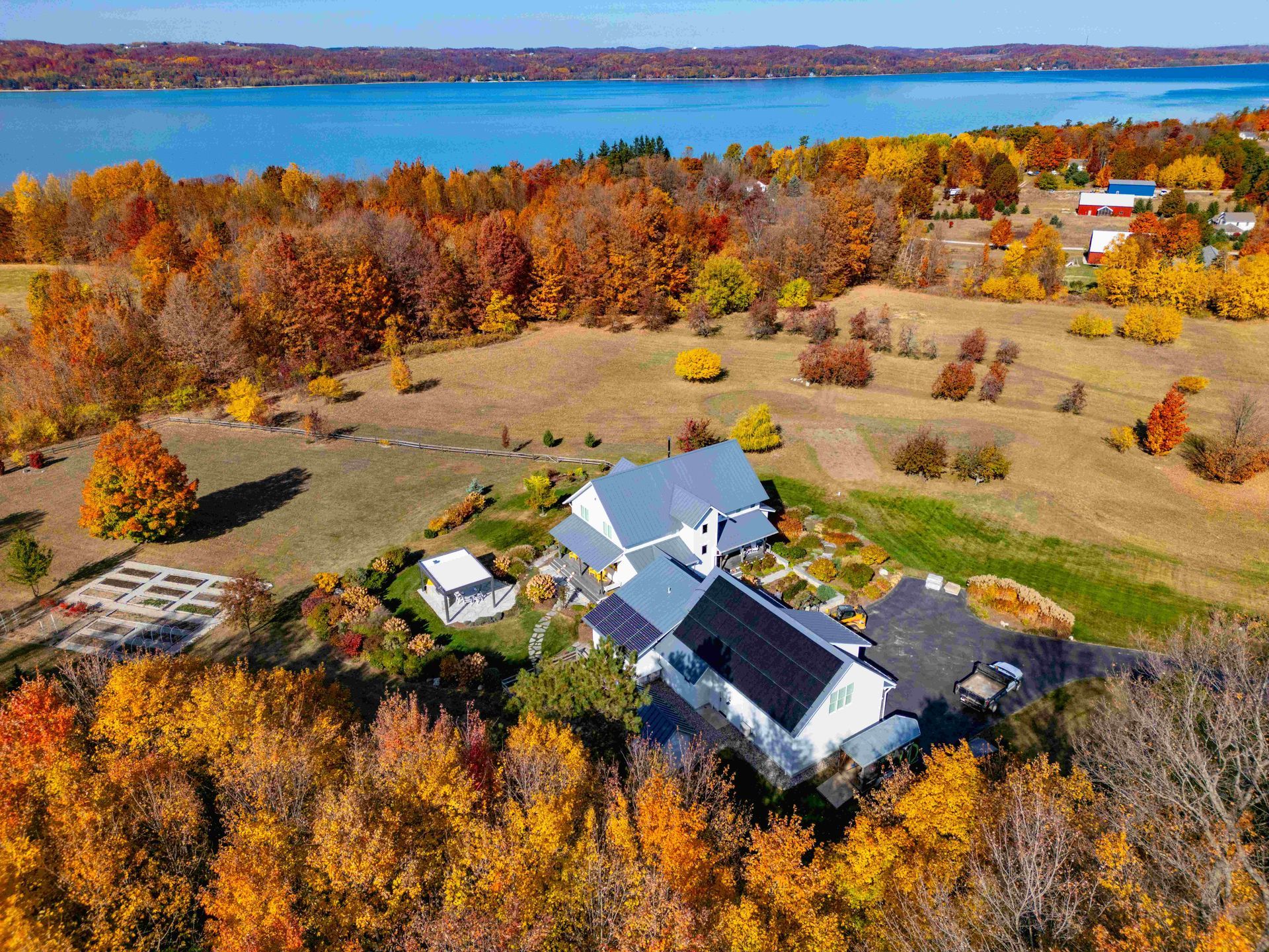 Aerial view of a white farmhouse with solar panels, nestled among vibrant autumn foliage overlooking a large blue lake.