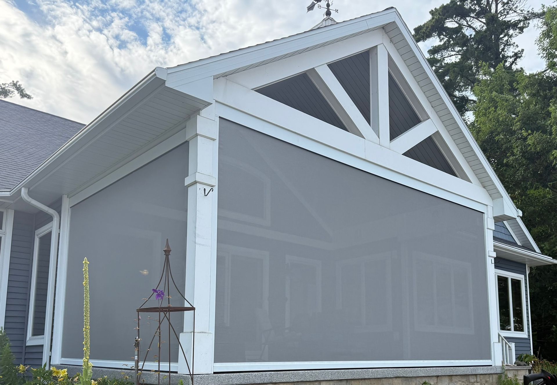 A gray retractable screen installed on the side of a blue house with a gabled porch roof.