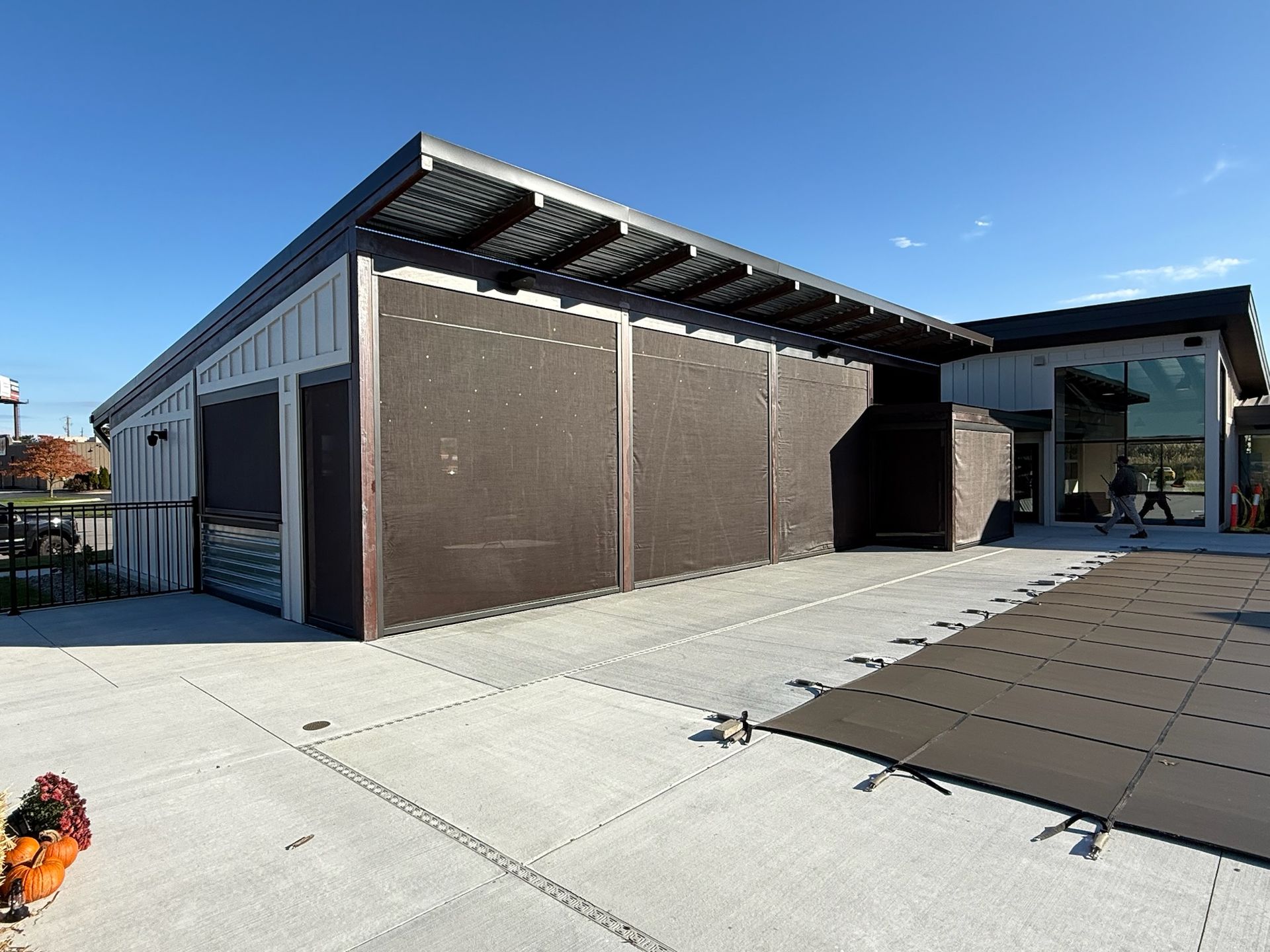 A modern building with a large covered patio and dark, retractable screens, set against a bright, clear blue sky.