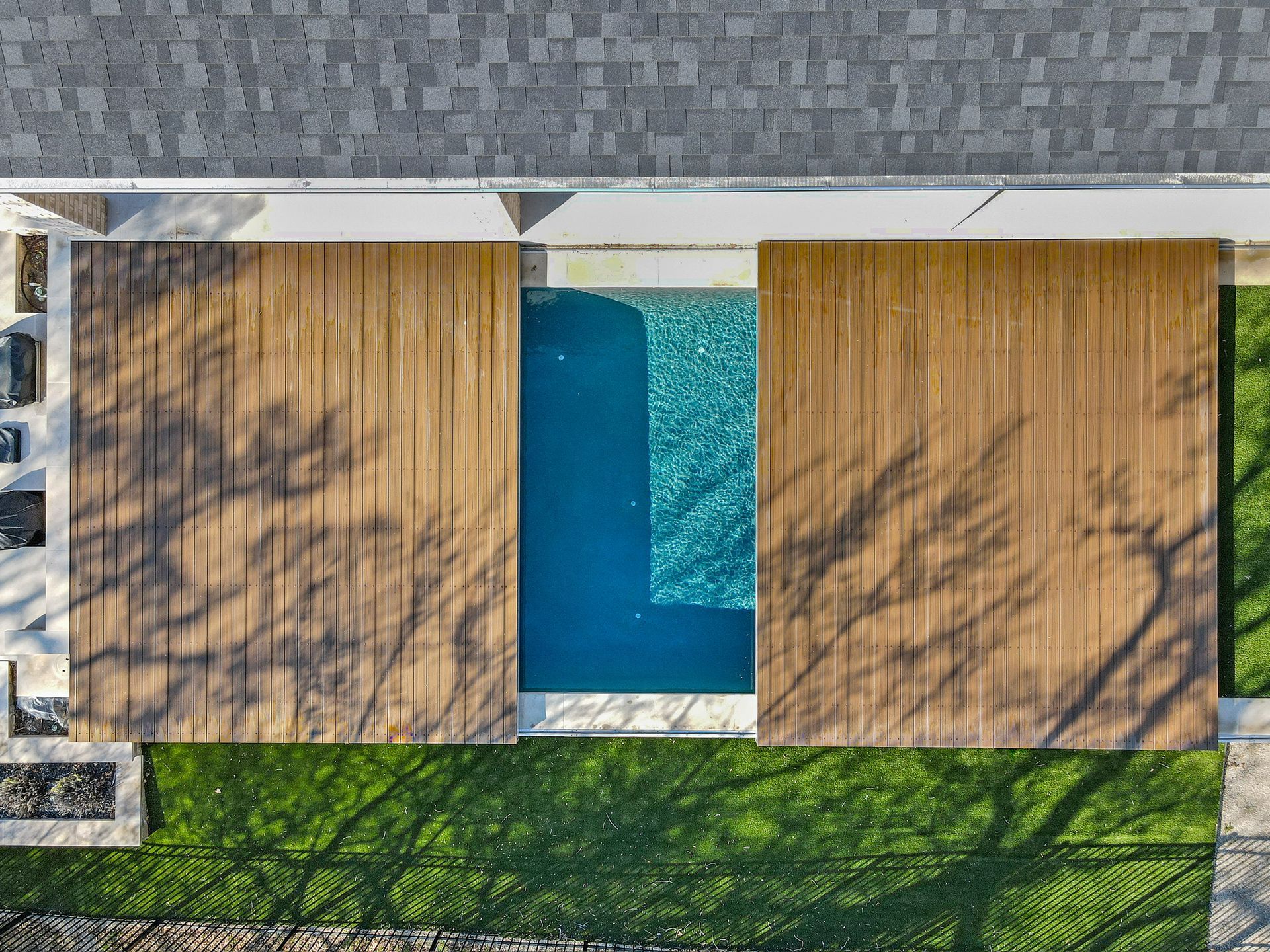 An overhead view shows a rectangular pool centered between two wooden decks, surrounded by grass and a stone patio.