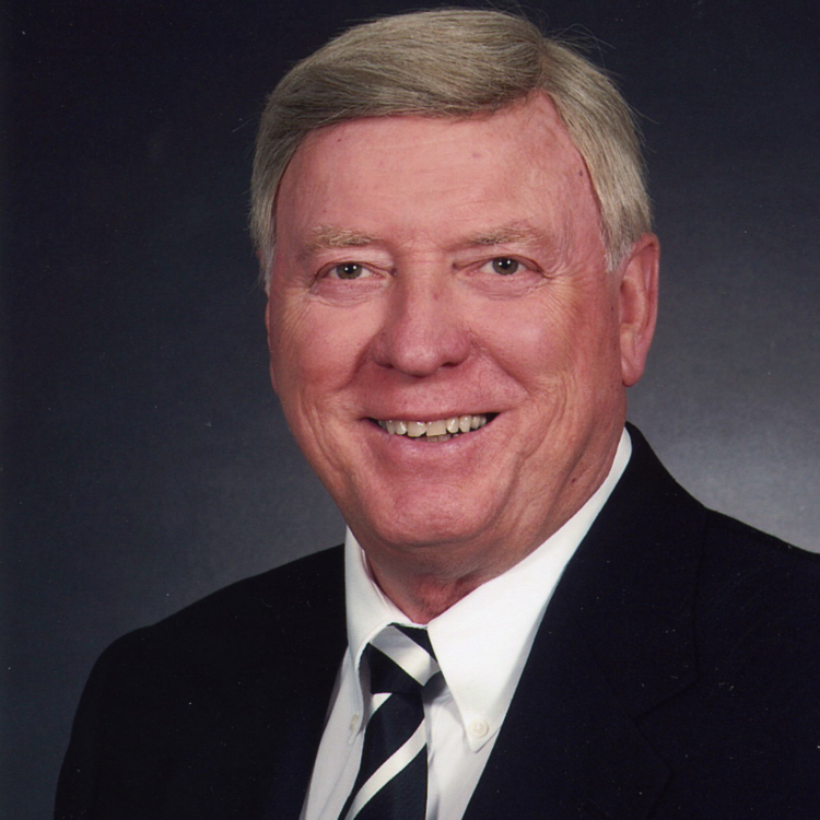 Studio portrait of a smiling man in a dark suit and striped tie on a gray background
