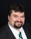 Portrait of a smiling man in a suit, white shirt, and green striped tie on a black background