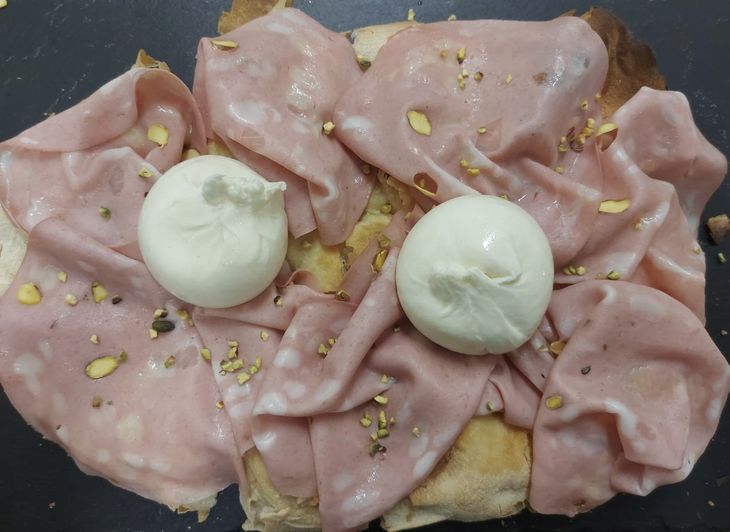 Sandwich aperto farcito con affettati rosa piegati, due palline di mozzarella e spezie sparse.