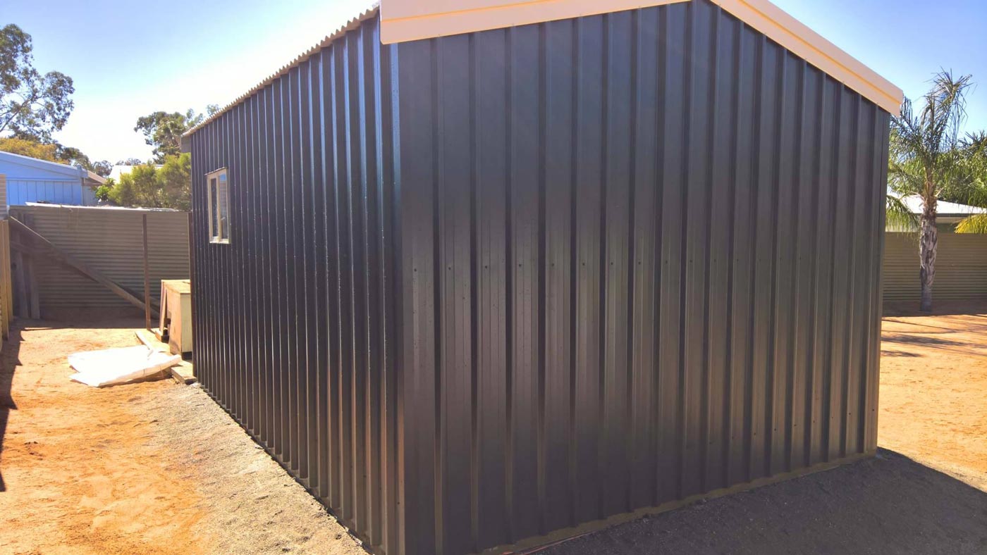 A Black Metal Shed With A White Roof Is Sitting On Top Of A Dirt Field — Alice Sheds & Structures In Ciccone, NT