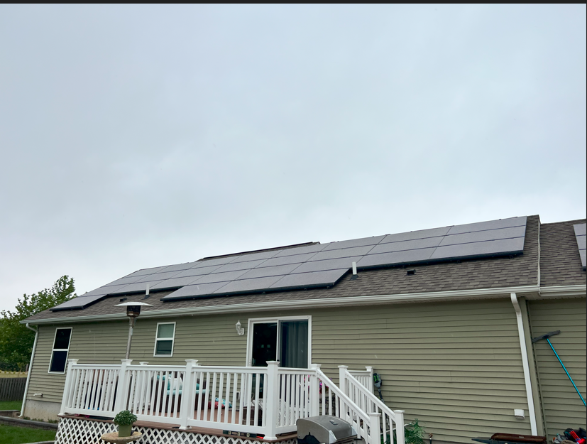 House with solar panels on the roof and a white front porch railing under a cloudy sky