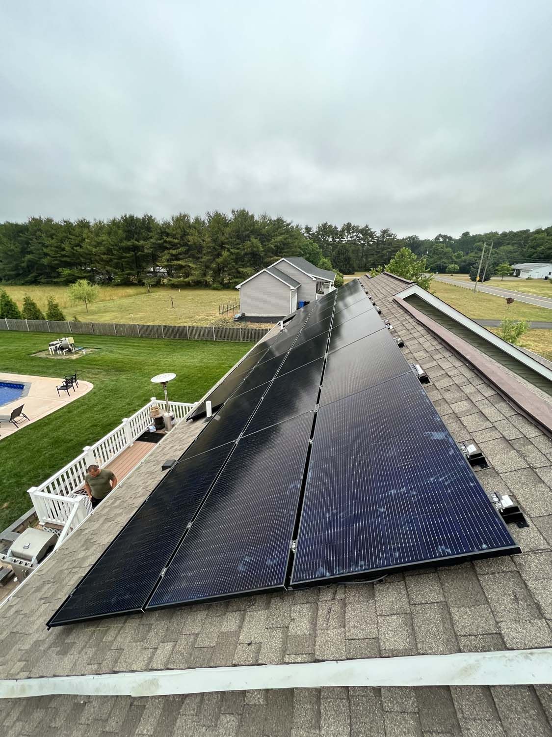 Solar panels on a rooftop under cloudy sky, overlooking a grassy yard and trees
