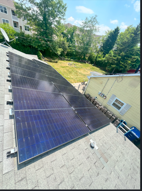 Solar panels installed on a roof beside a house and trees on a sunny day