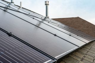 Solar panels on a sloped rooftop beside a chimney under a cloudy sky