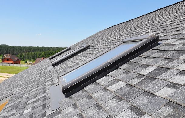 Sloped gray shingle roof with a skylight window under a clear blue sky