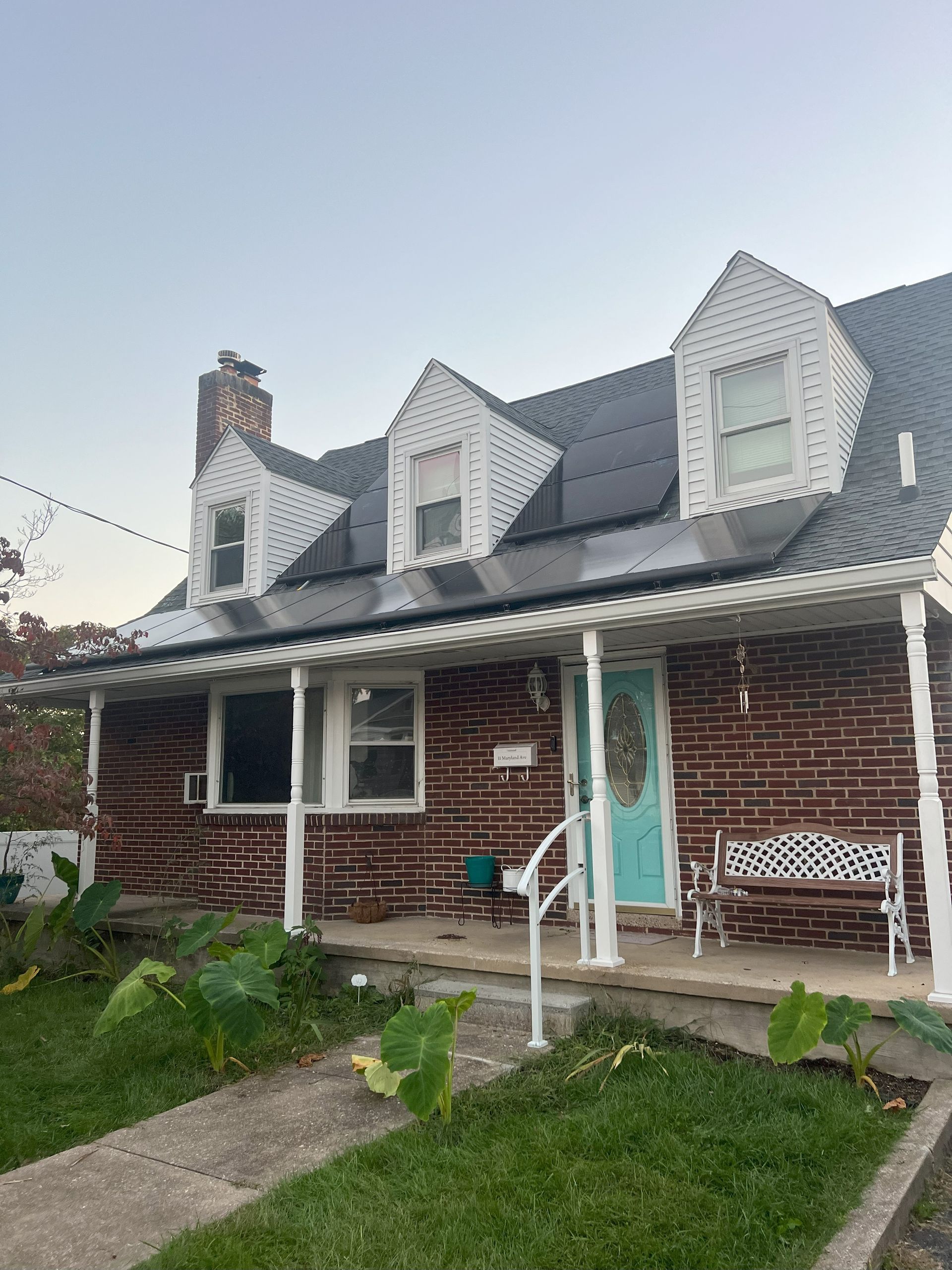 Brick house with gray roof, white trim, and turquoise front door under a cloudy sky