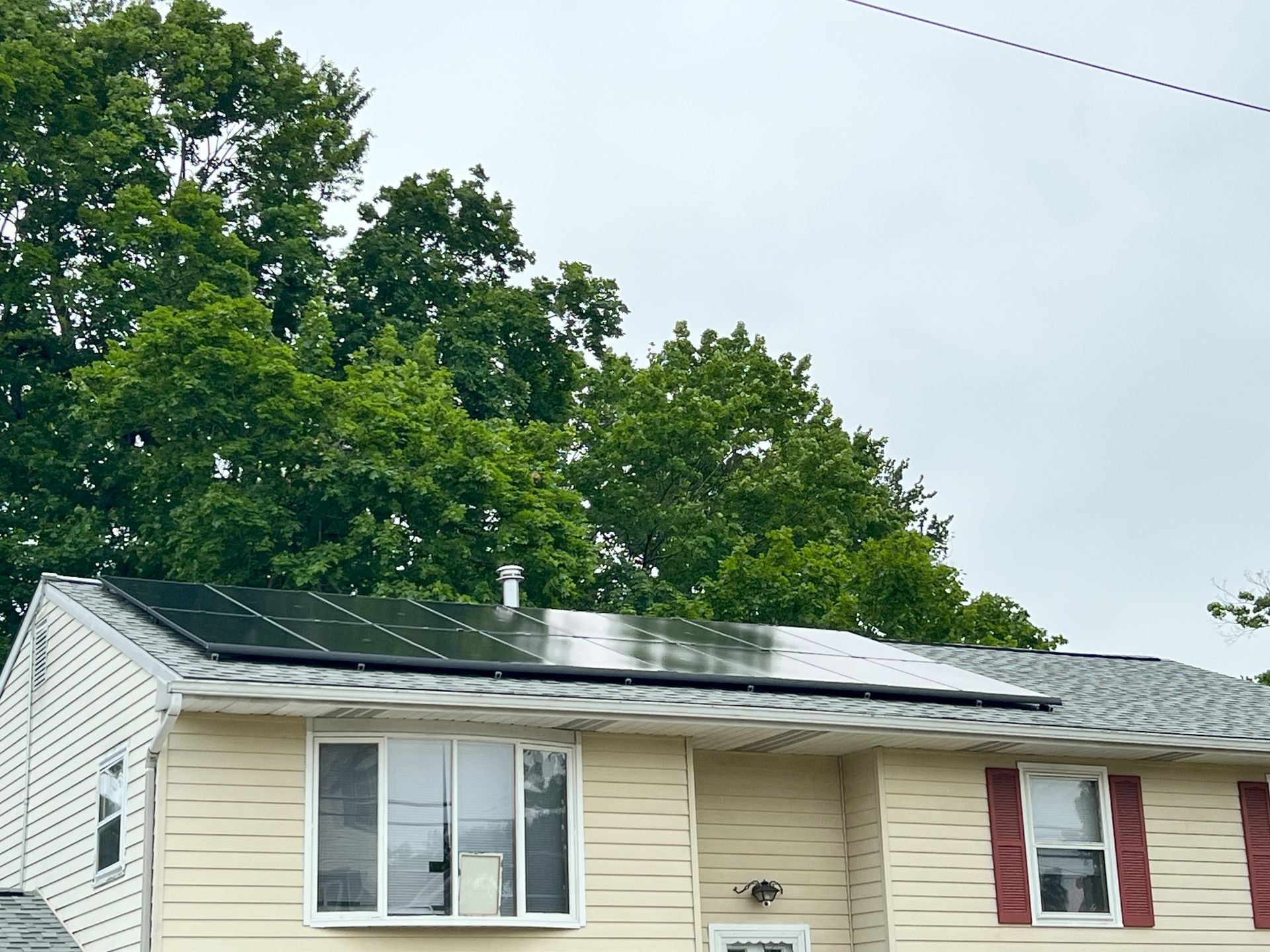 Single-story house with green and white siding, roof solar panels, and large trees behind it
