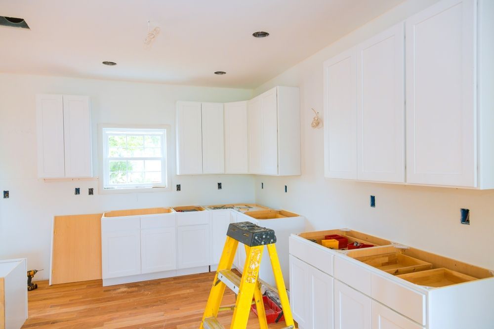 Bright unfinished kitchen with white cabinets, wood floor, and a yellow step ladder in the center.