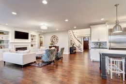Spacious open-plan living room with white sofas, fireplace, TV, staircase, and hardwood floors