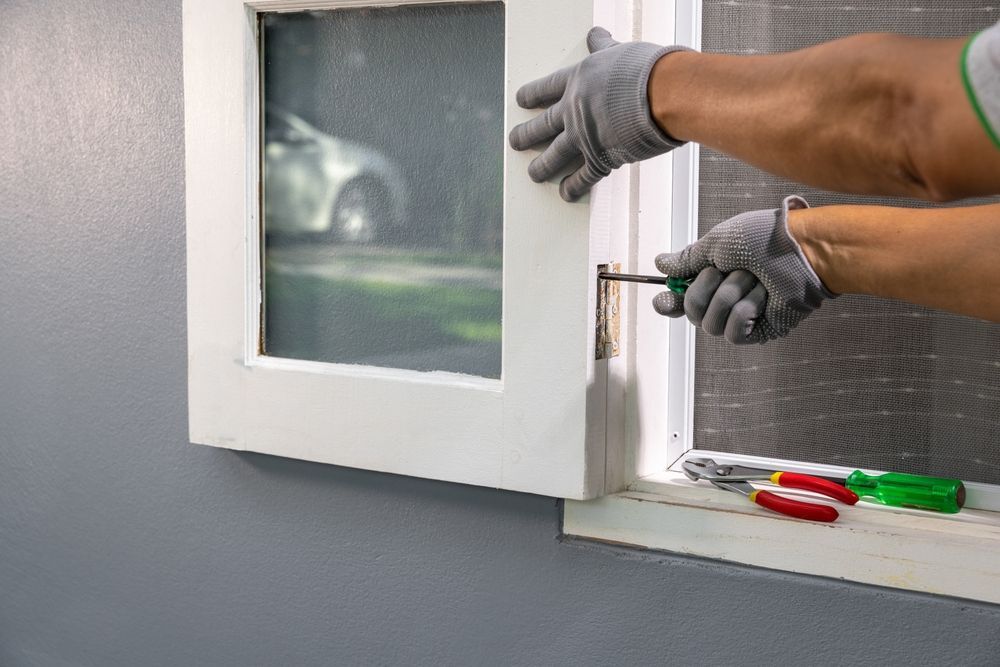 Gloved hands using a screwdriver to install a white window frame outdoors