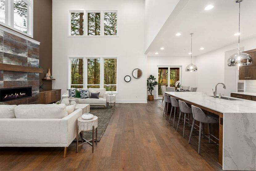 Modern open-concept living room and kitchen with white furniture, wood floors, and large windows