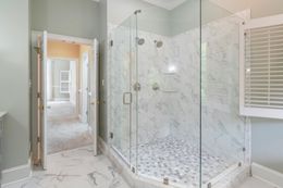 Bright bathroom with glass shower, marble tile, and open doorway to a hall with white shutters.