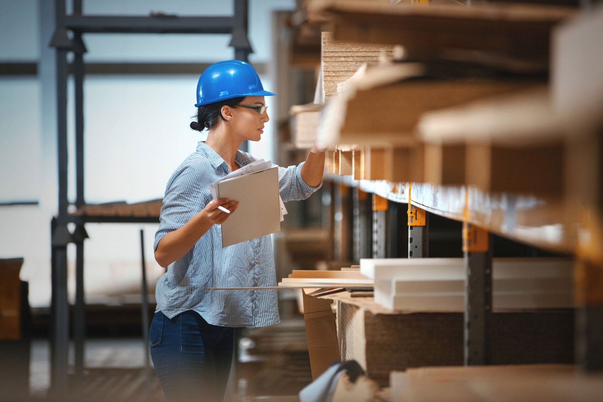 A woman in a hard hat is looking at a clipboard in a warehouse. A woman in a hard hat is looking at a clipboard in a warehouse.