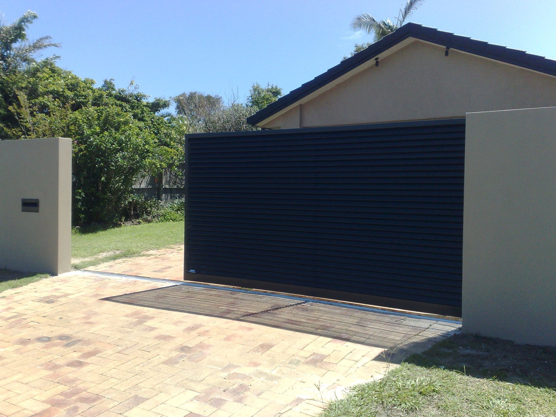 Black Sliding Gate in Front of a Beige House — Coastal Auto Doors & Gates In Palmwoods, QLD