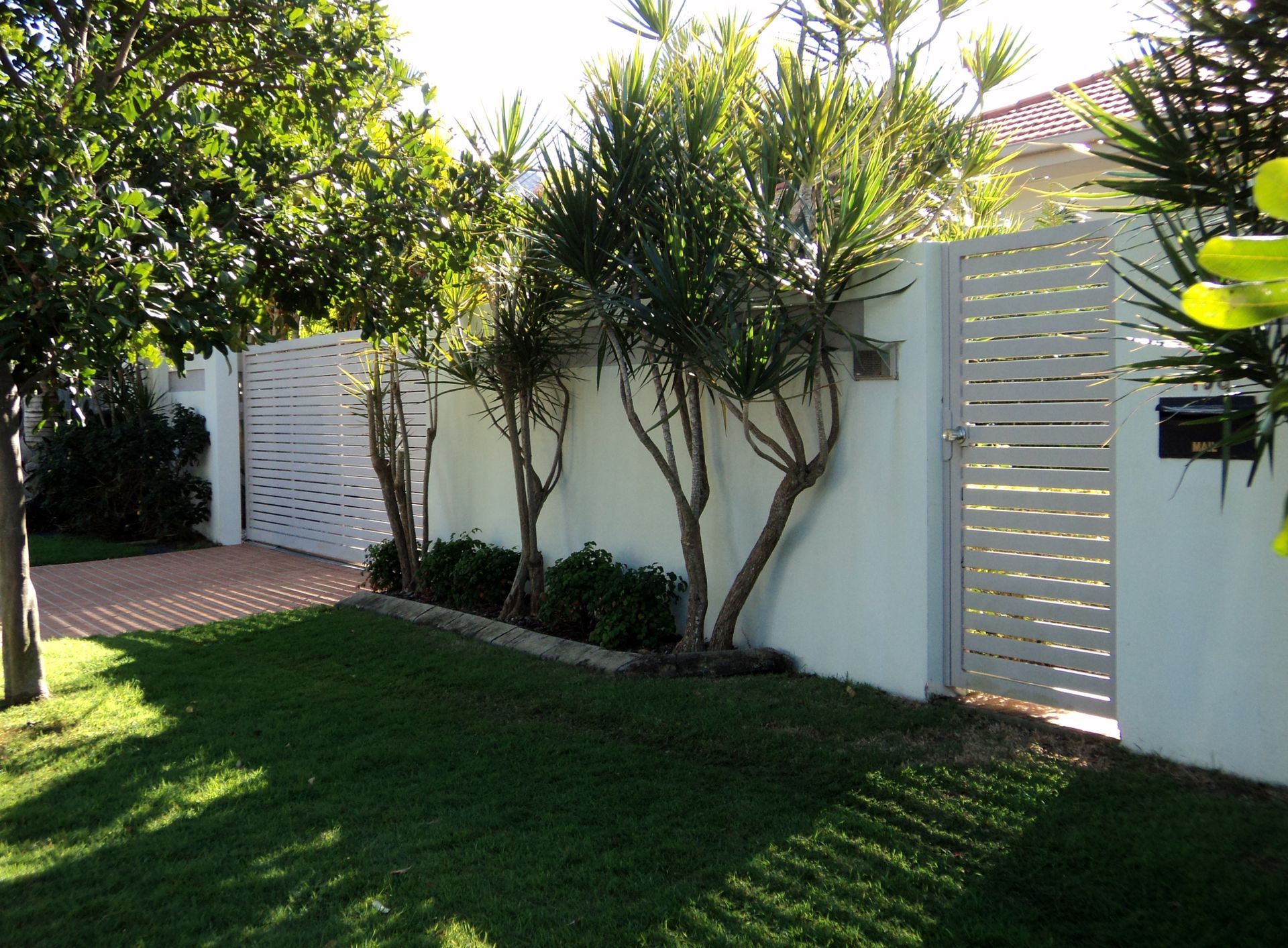 White Slatted Fence and Gate With Green Lawn and Trees — Coastal Auto Doors & Gates In Palmwoods, QLD