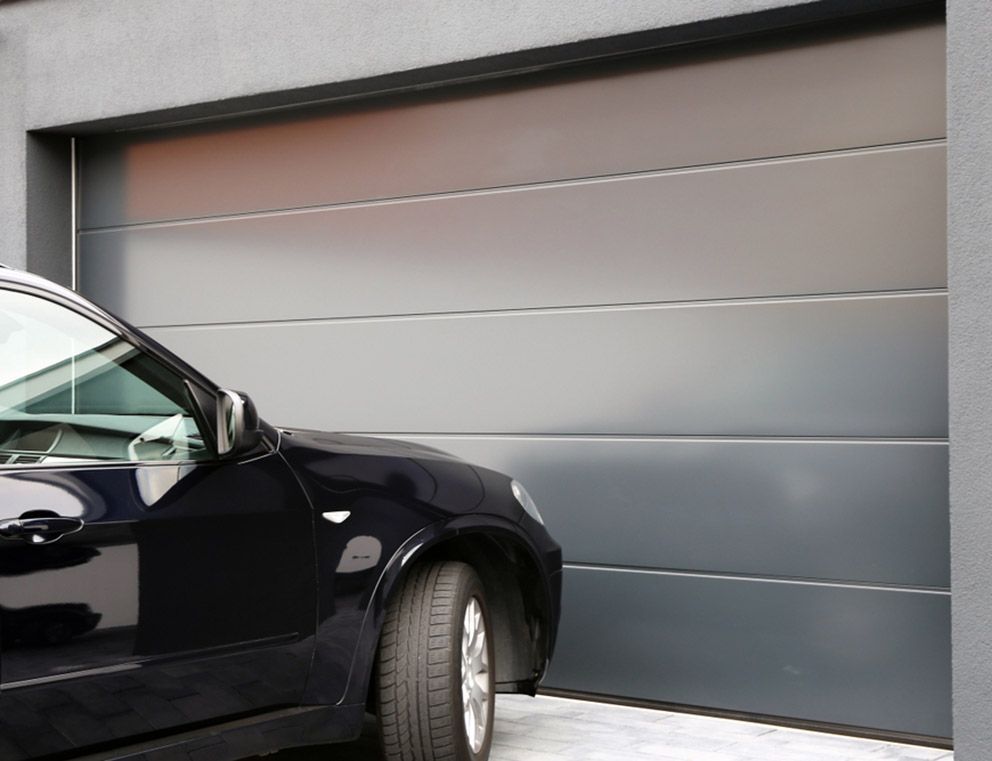 A Car Pulling up to A Grey Panelled Garage Door — Coastal Auto Garage Doors & Gates In Burpengary, QLD