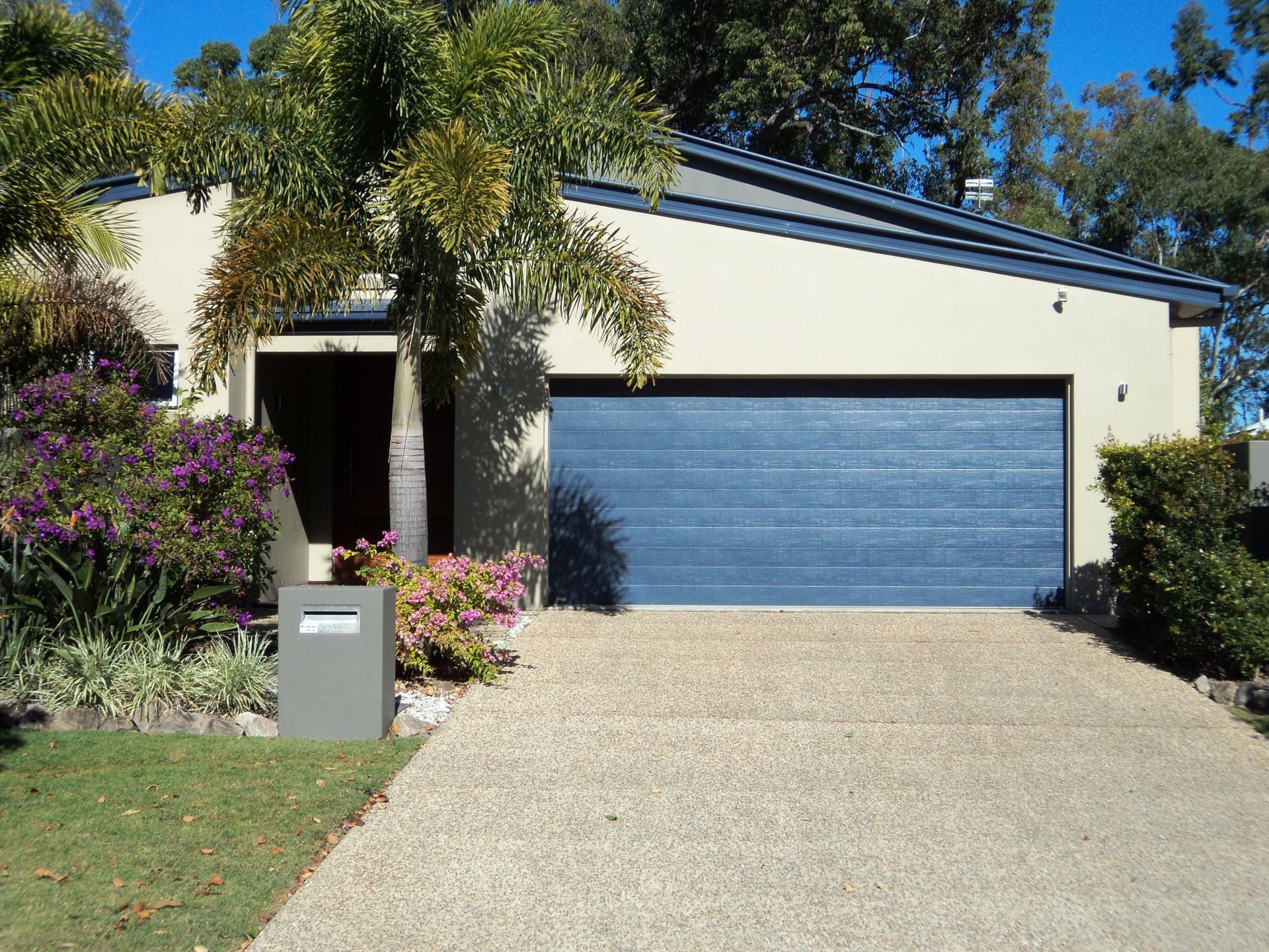House with blue garage door and concrete driveway on a sunny day. — Coastal Auto Doors & Gates In Palmwoods, QLD