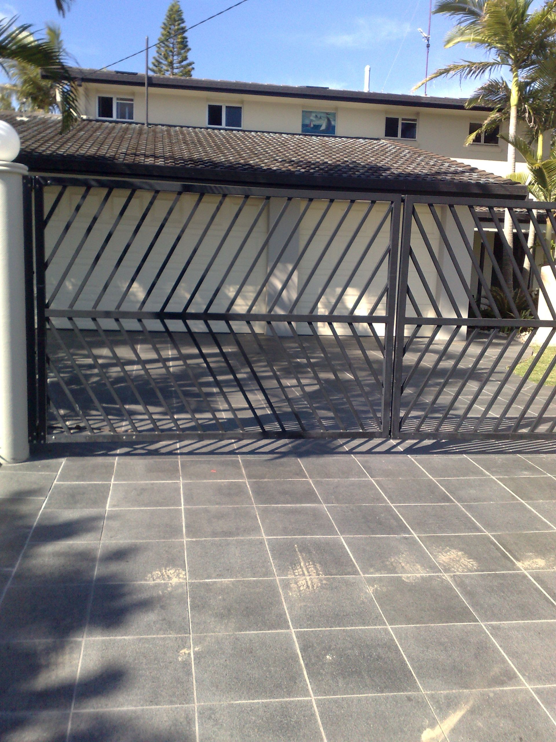 Black Metal Gate in Front of a House, With Gray Tiled Driveway and Sunny Sky — Coastal Auto Doors & Gates In Palmwoods, QLD