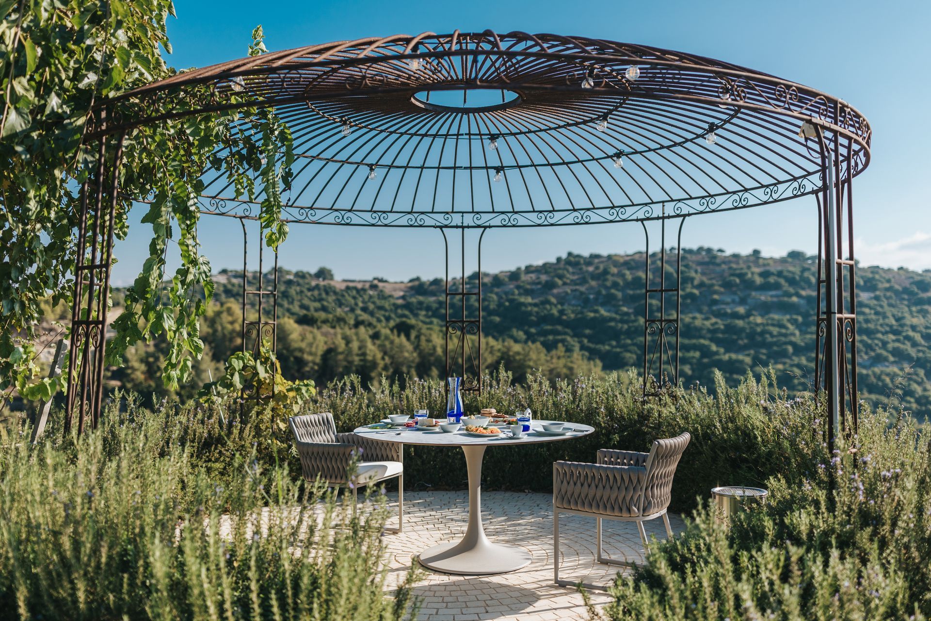 Outdoor dining area with a round metal pergola, table, chairs, and scenic view.