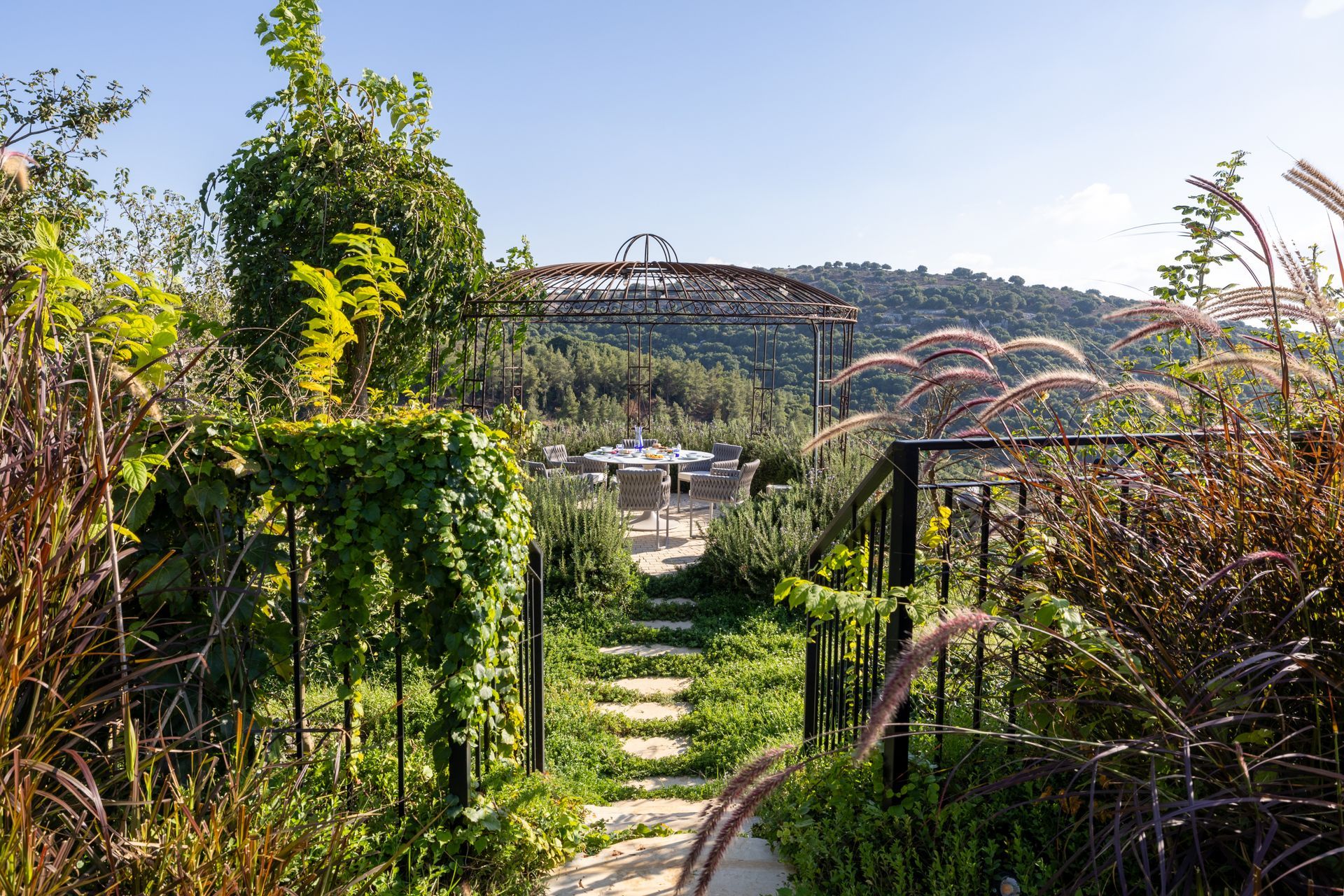 Stone path leads through a garden, toward a bridge structure and distant trees under a bright sky.