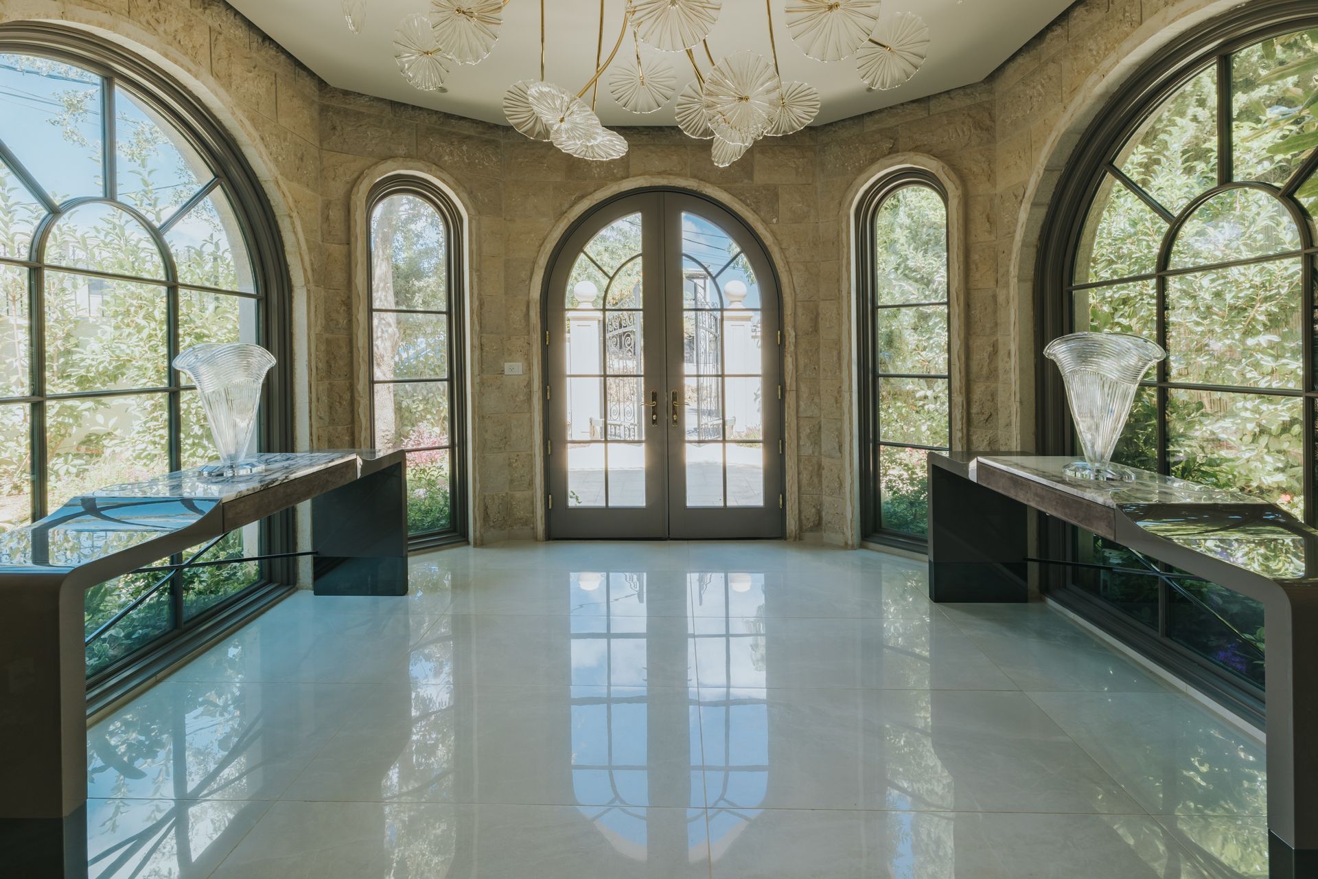 Grand foyer with arched windows, glass doors, and reflective white floor. Two long consoles flank windows.