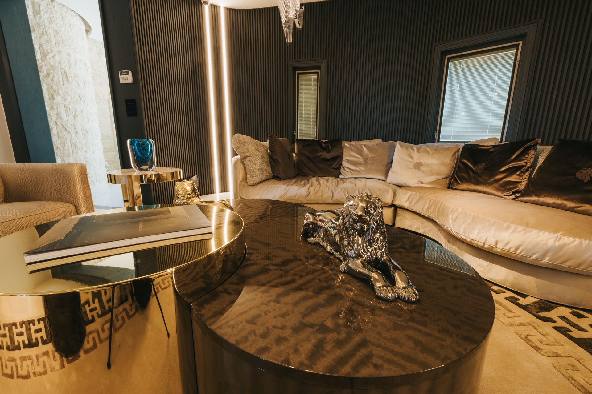 Luxurious living room with curved sofa, gold coffee table, and dark walls.