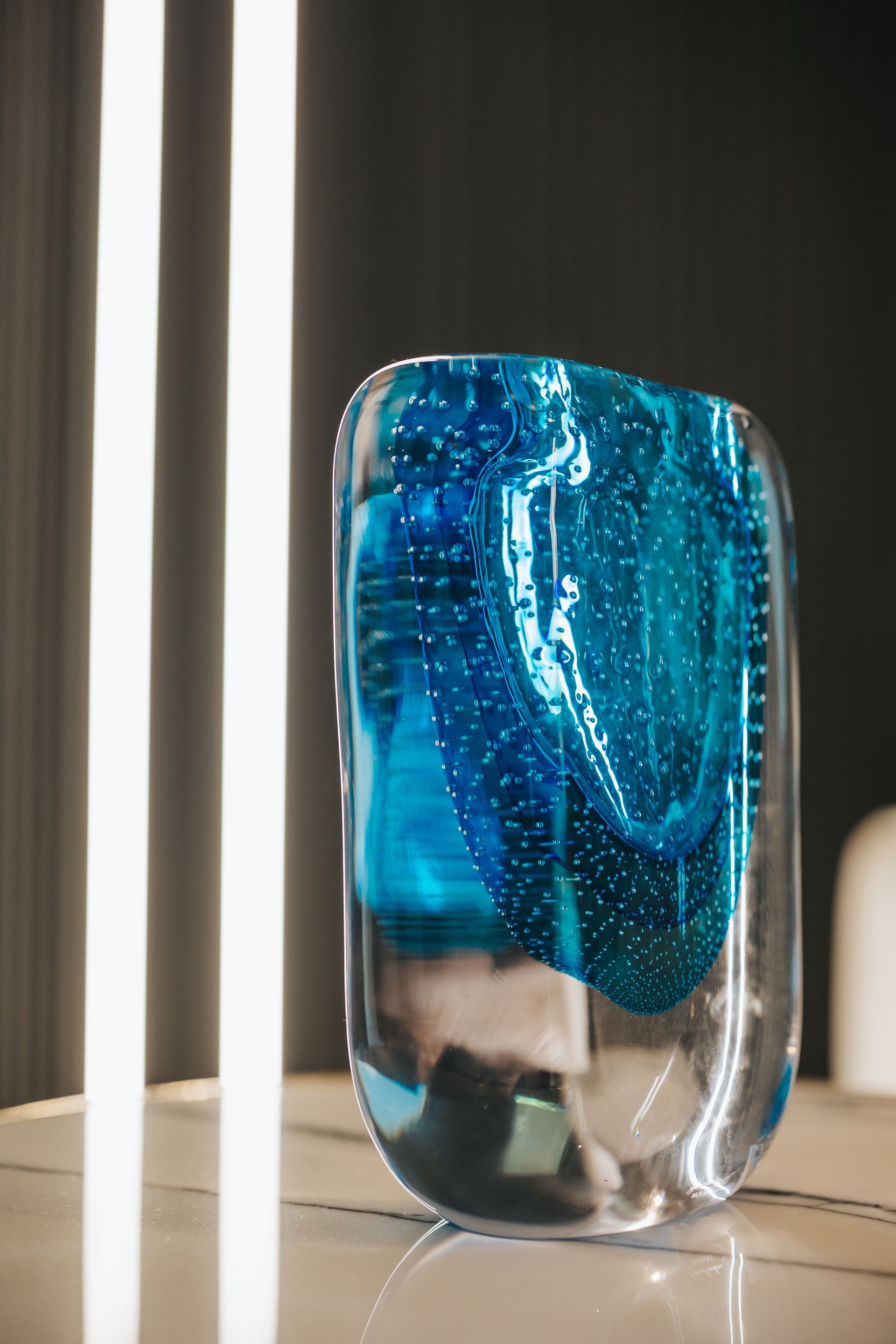 Clear glass vase with blue swirls, sitting on a marble surface, with vertical lights in the background.