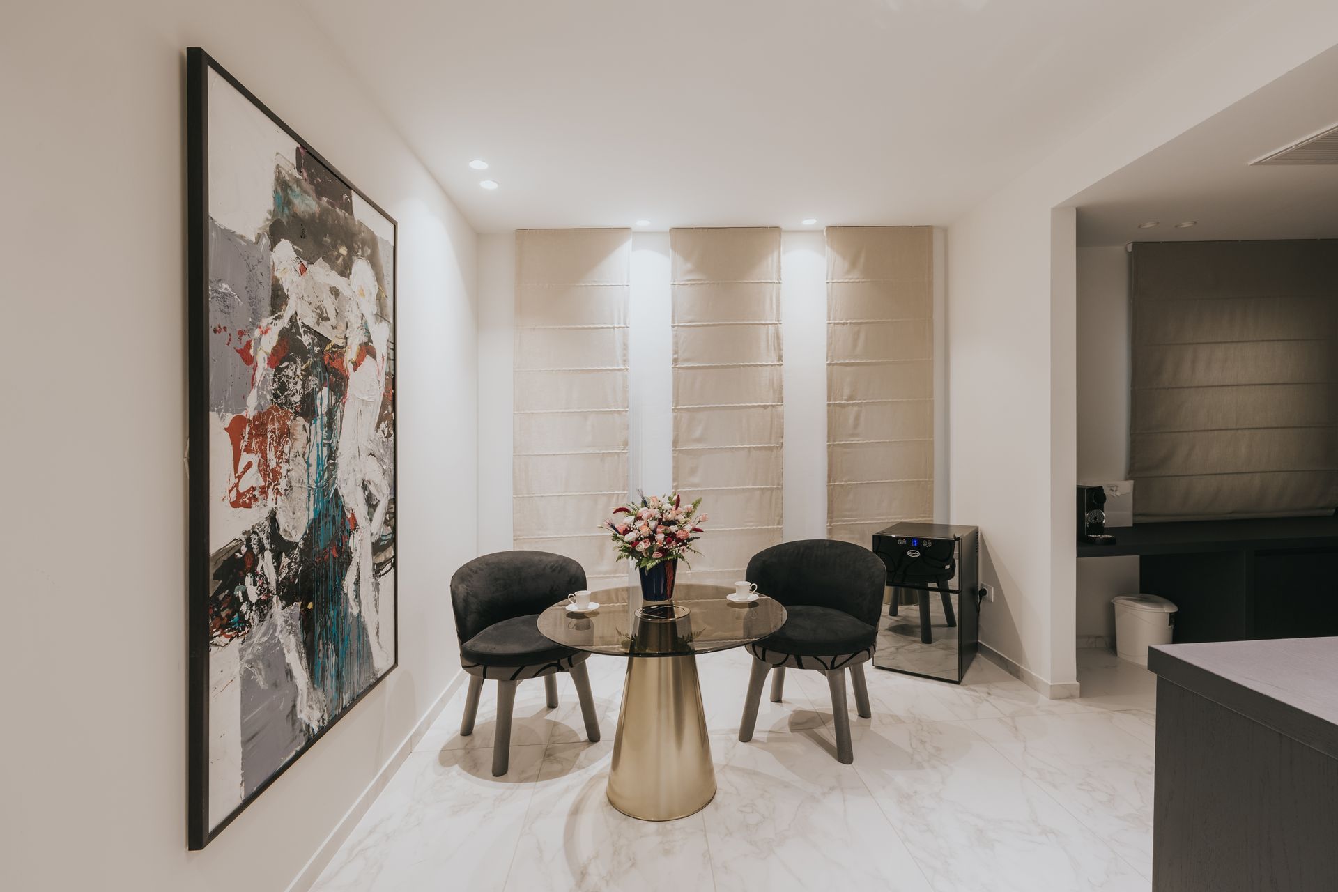 Small dining area with a round table, two black chairs, and art on the wall.