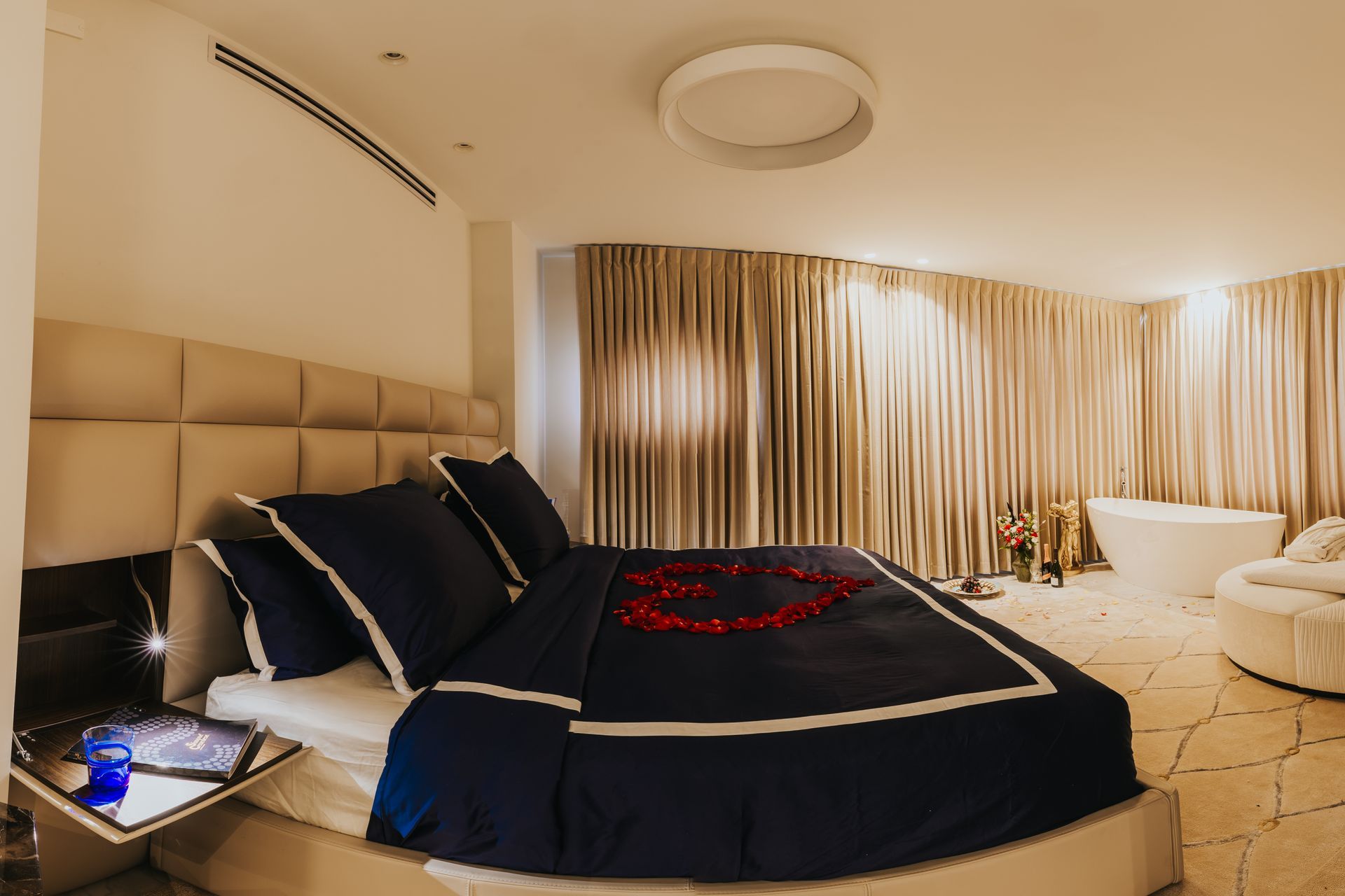 Luxurious bedroom with king bed, navy bedding, rose petals, and a freestanding tub.