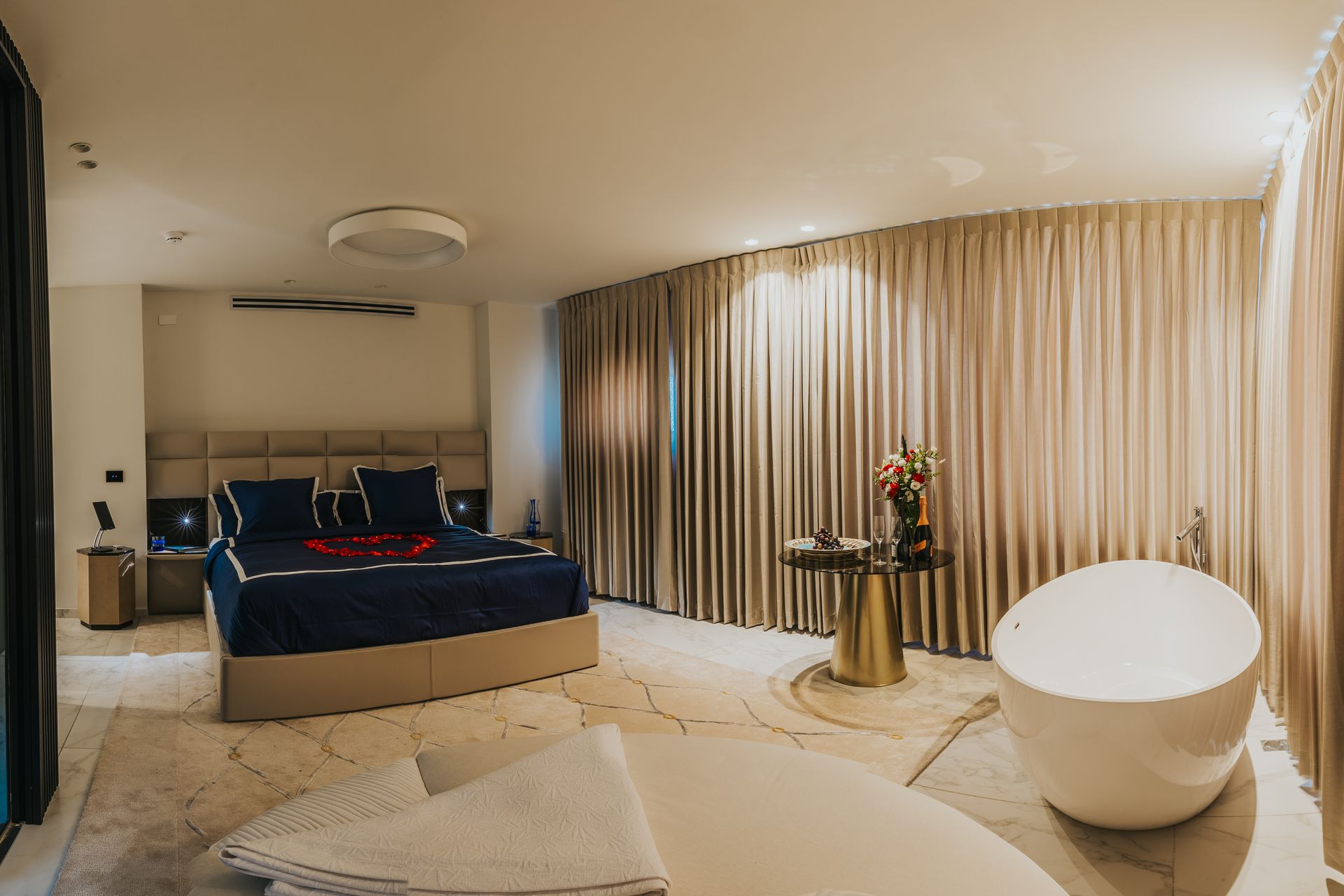 Luxurious bedroom with king bed, freestanding tub, and elegant gold curtains.