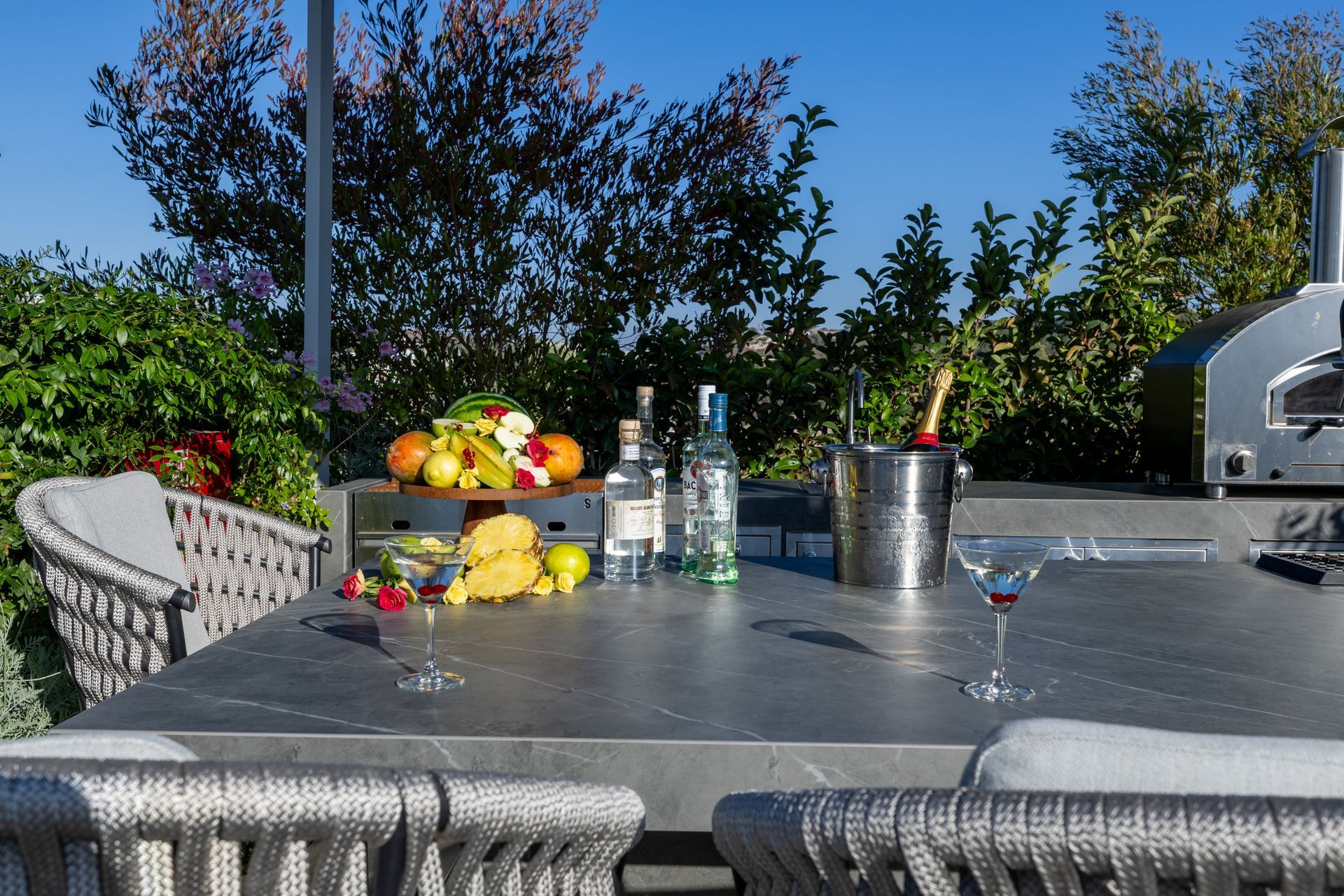 Outdoor bar with fruits, liquor, champagne, and a pizza oven.