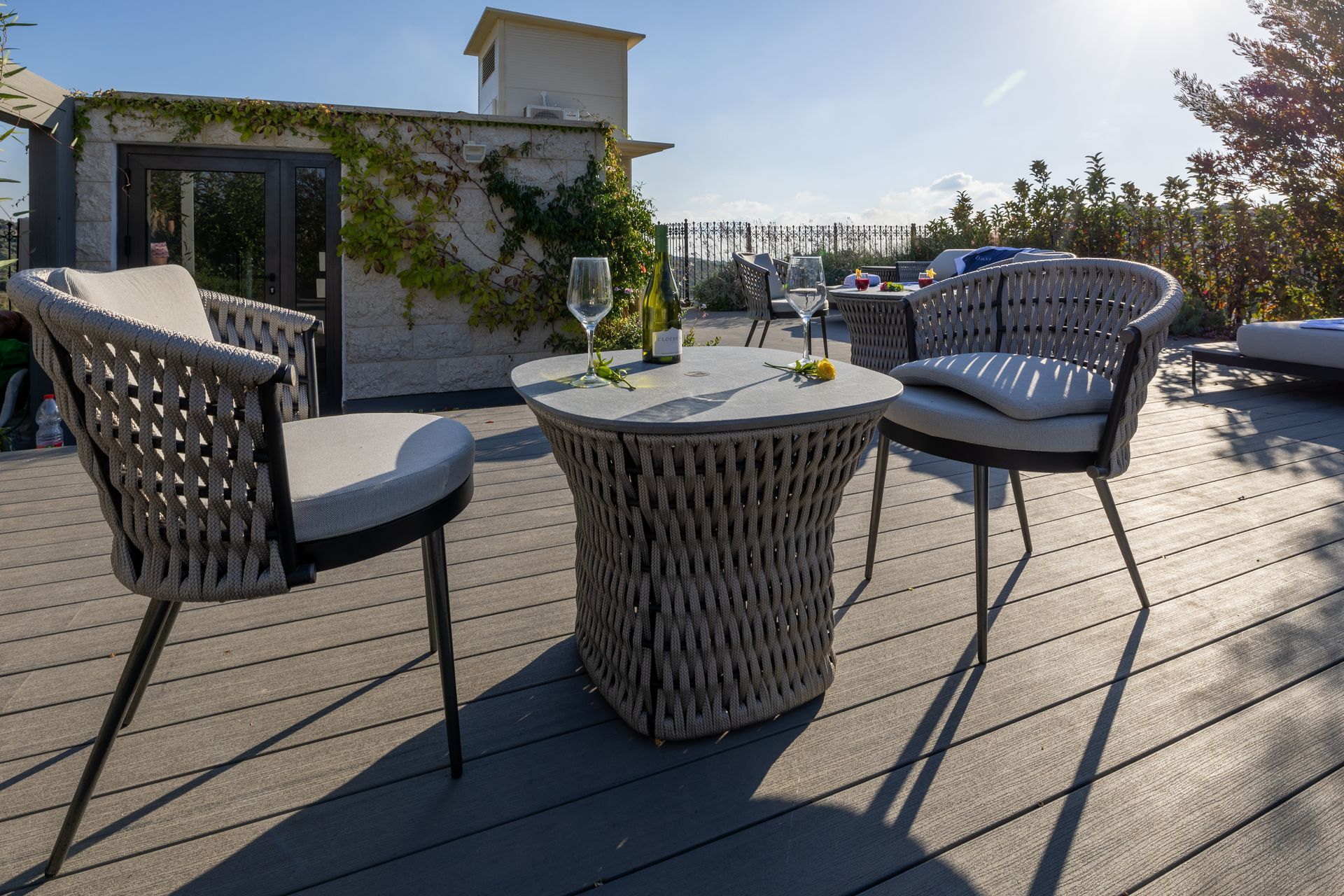 Patio set with woven chairs and small table on a deck with building in the background.