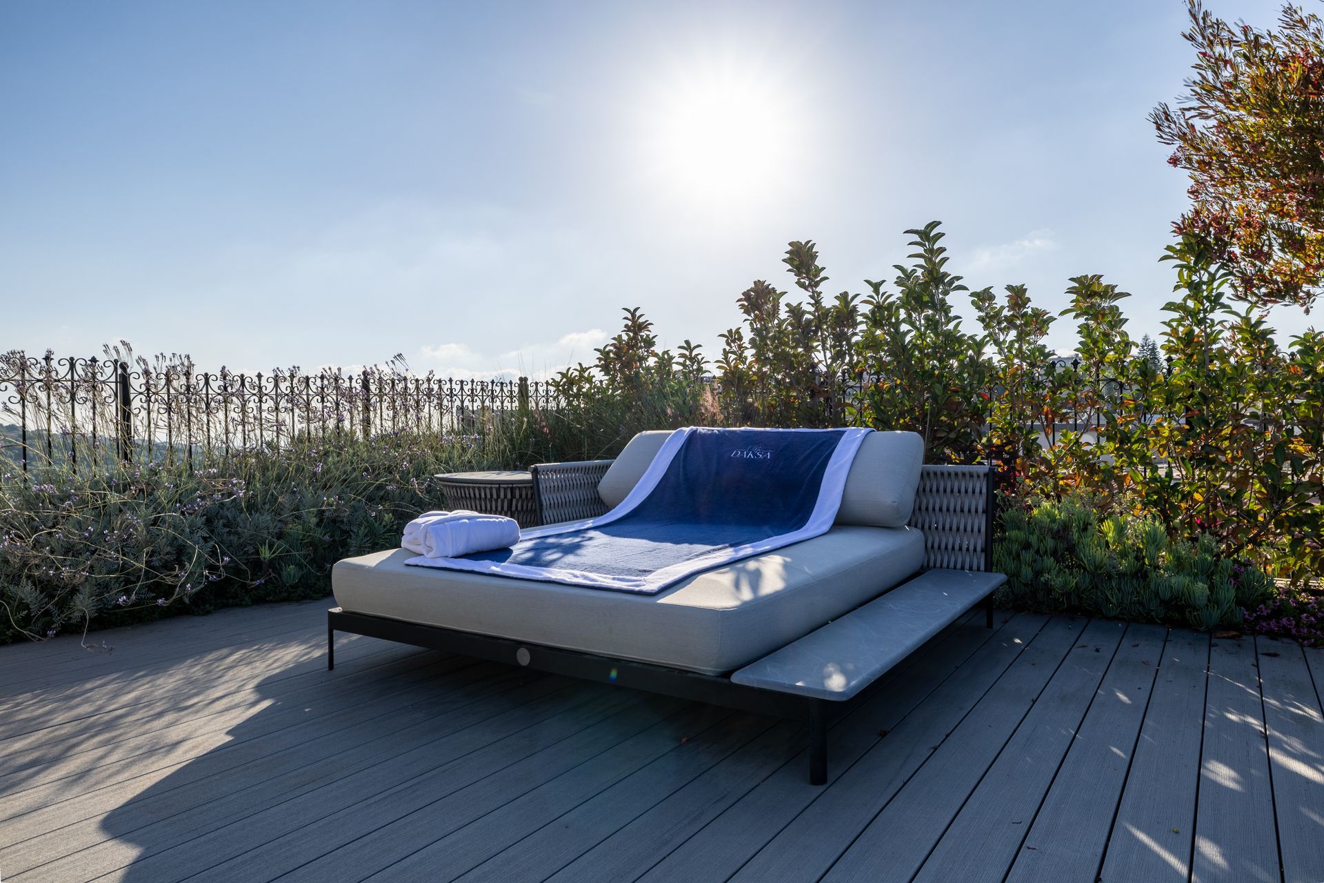 Sun deck with lounge chair, towel, foliage, and sunlight.