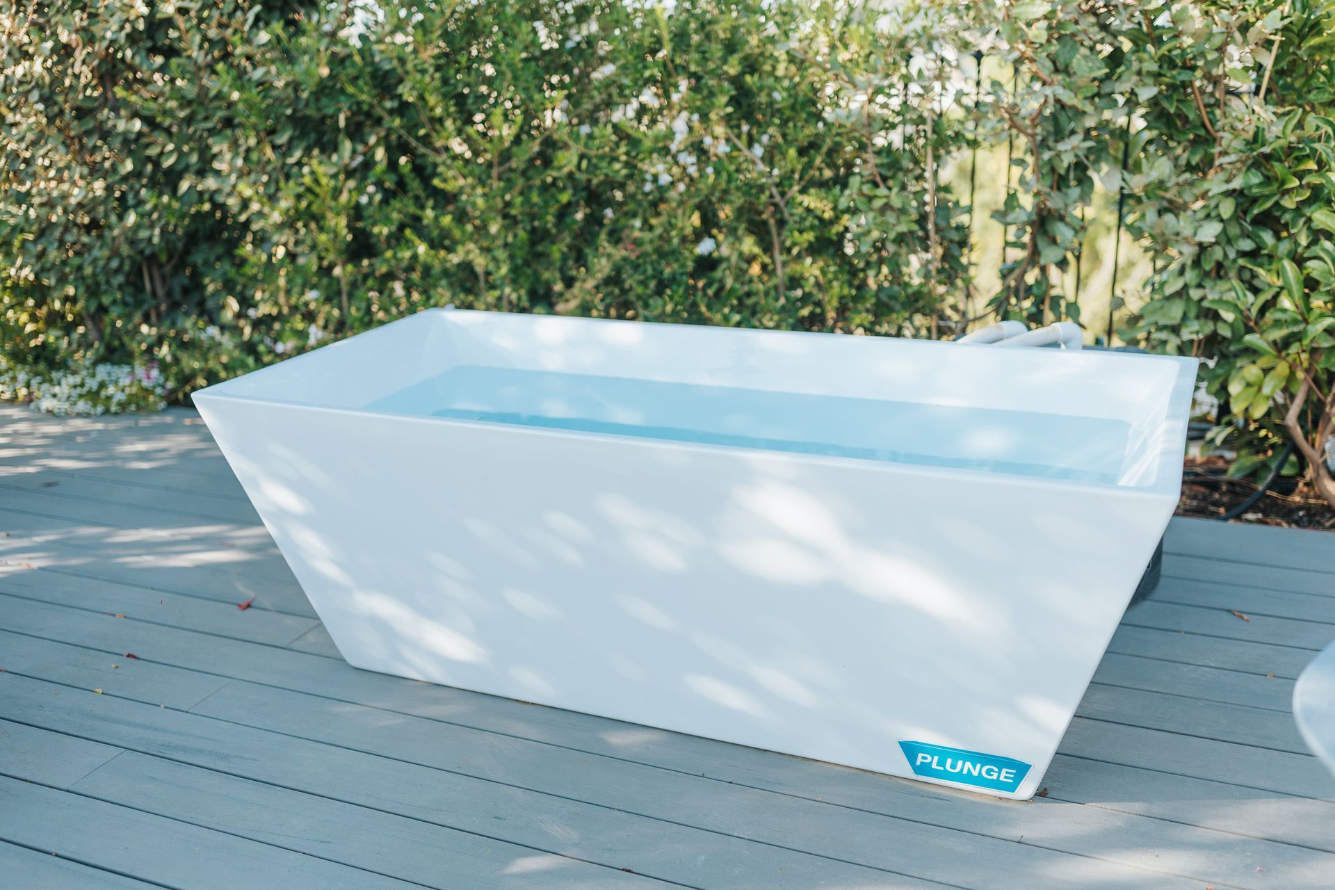 White ice bath tub filled with water, on a wooden deck outdoors. Blue logo on side.
