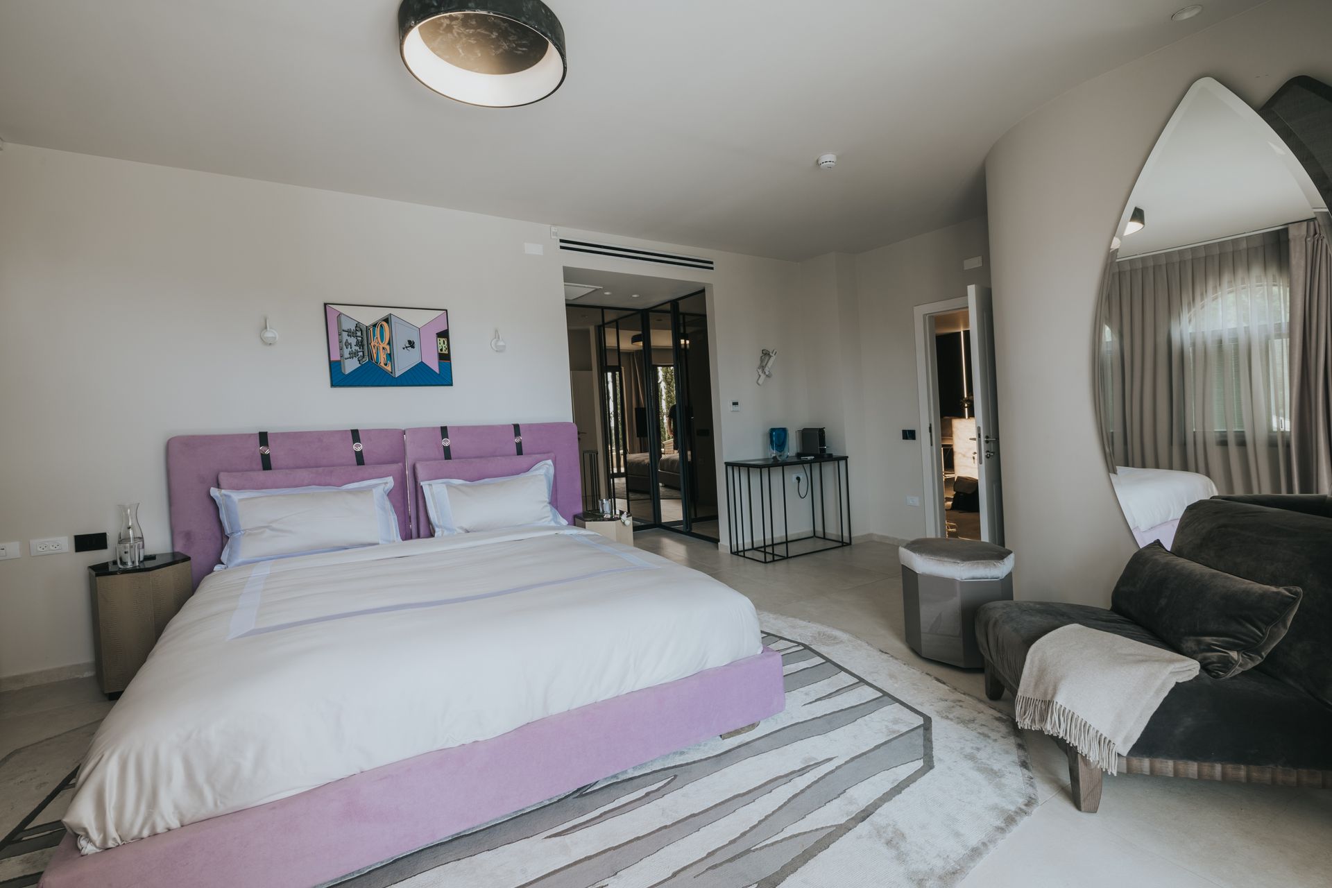 Bedroom with lavender bed, large mirror, and seating area.