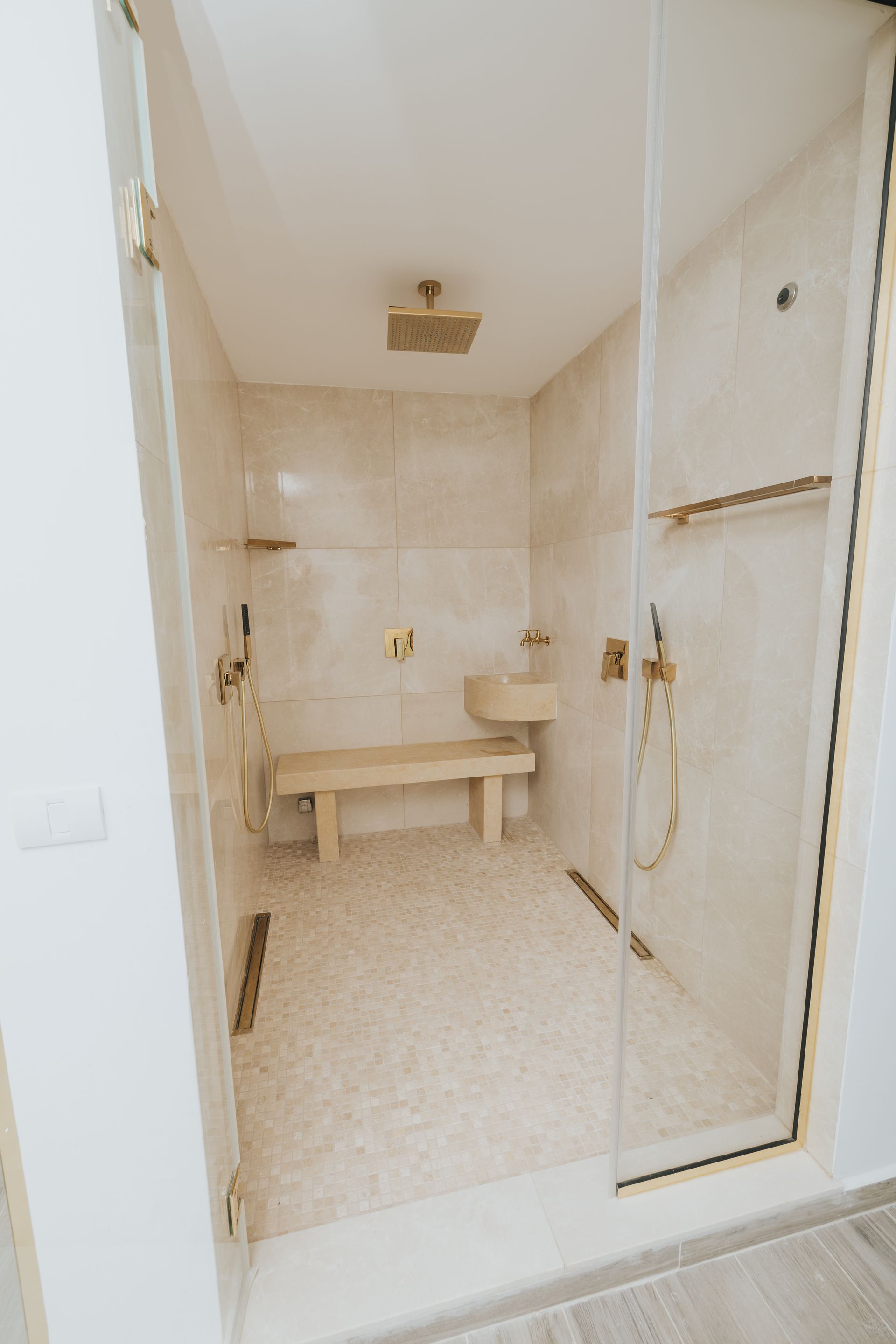 A luxurious, tiled walk-in shower with gold fixtures, a bench, and glass doors.