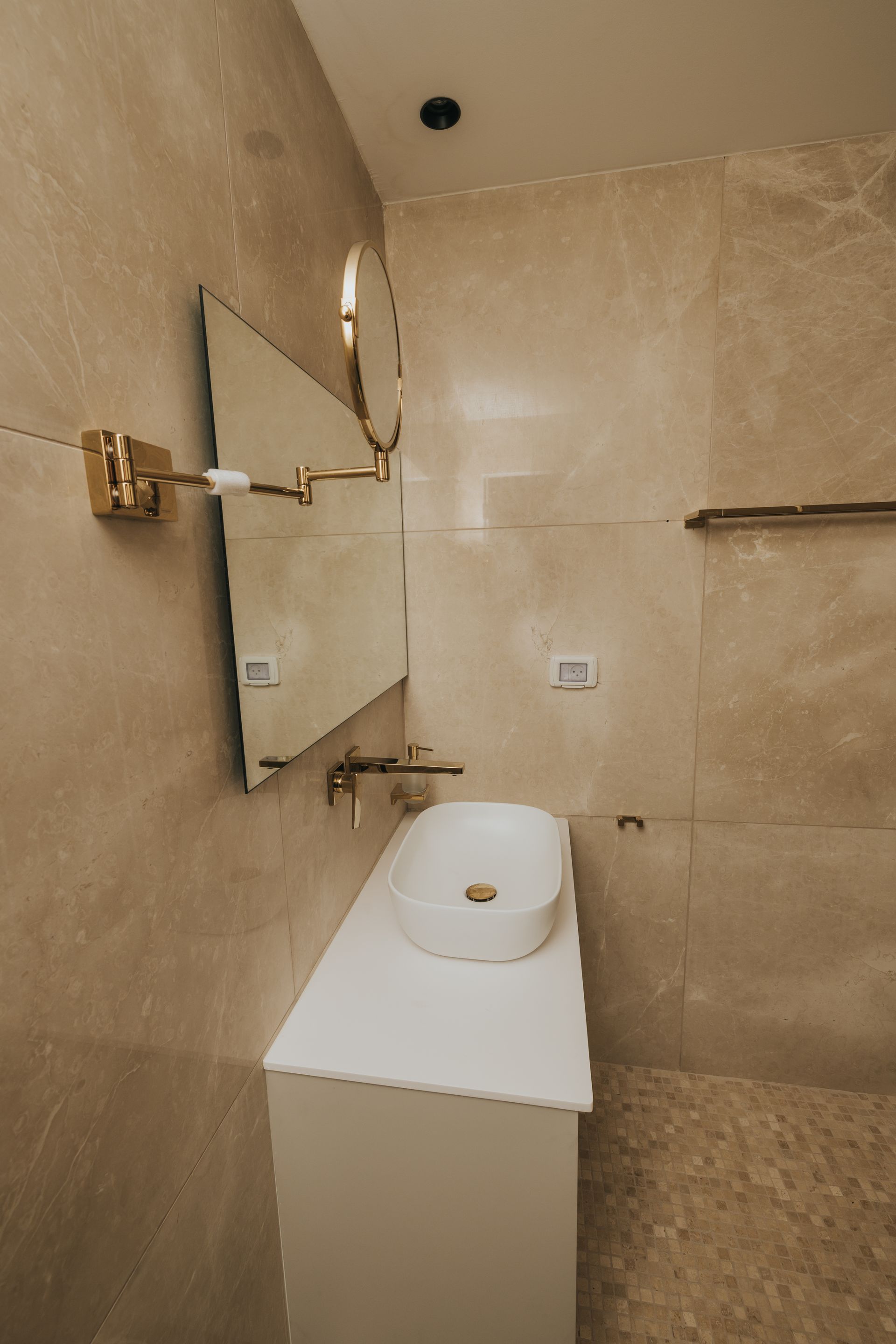 Modern bathroom with white vanity, vessel sink, gold fixtures, and marble-like tile.