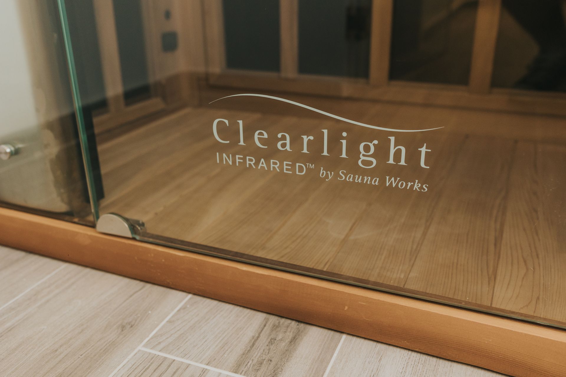 Close-up of a Clearlight Infrared sauna's glass door. The logo is visible on the glass. The sauna has a wooden frame.