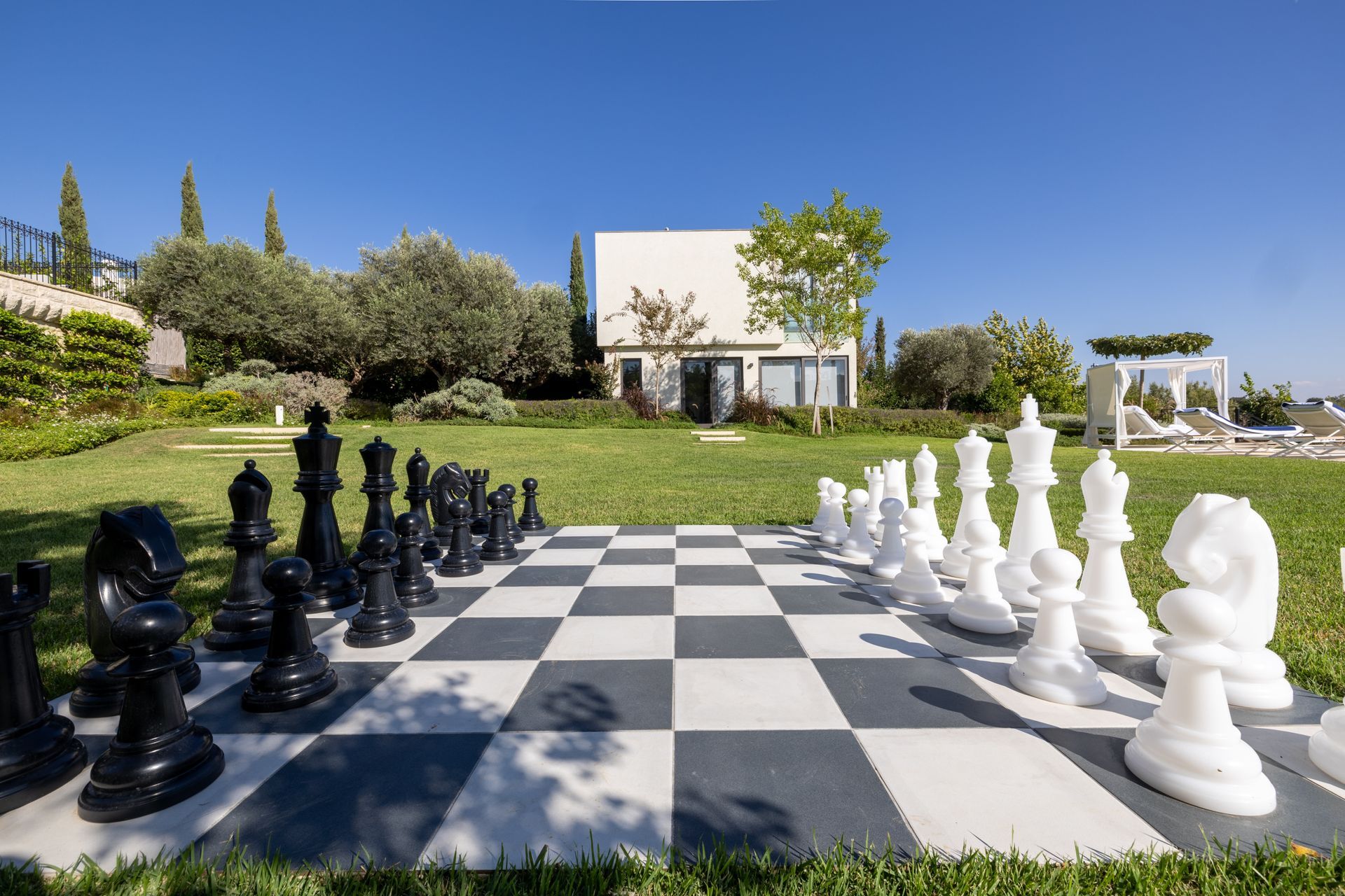 Large outdoor chess set on a checkered board in front of a white building on a sunny day.