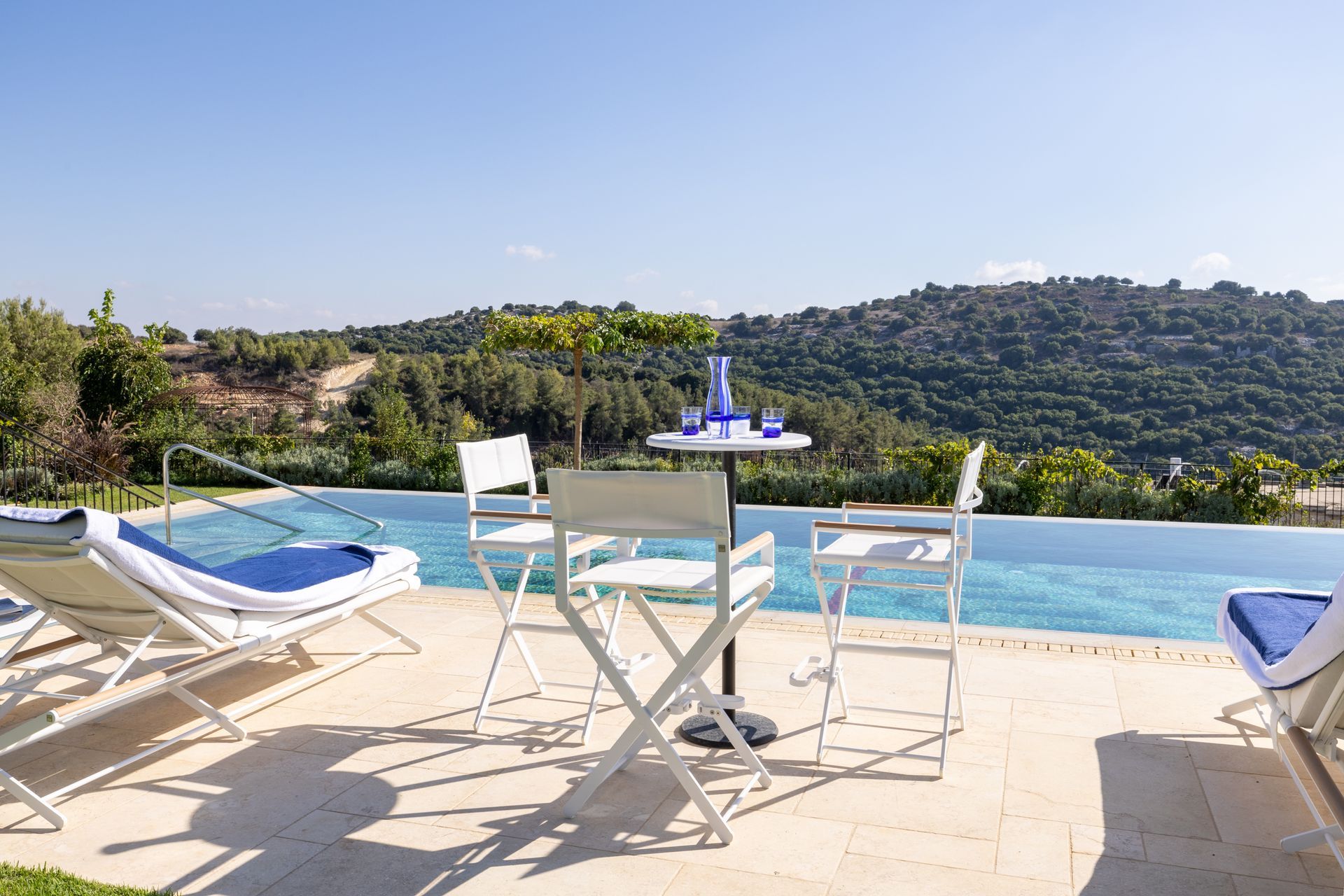 Poolside scene with white chairs, table, and blue accents, overlooking hills.