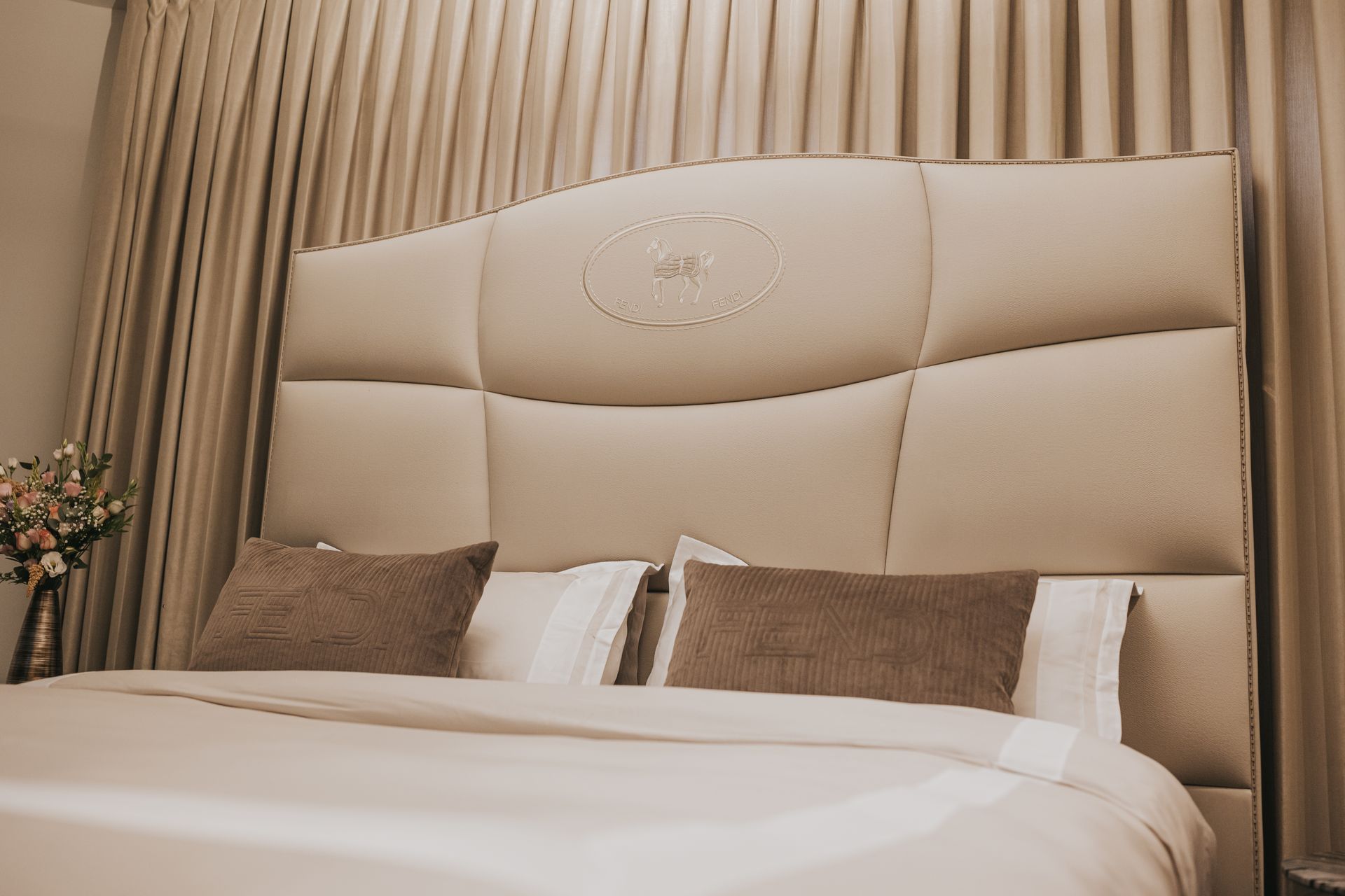 Beige upholstered bed with decorative headboard and two brown pillows.