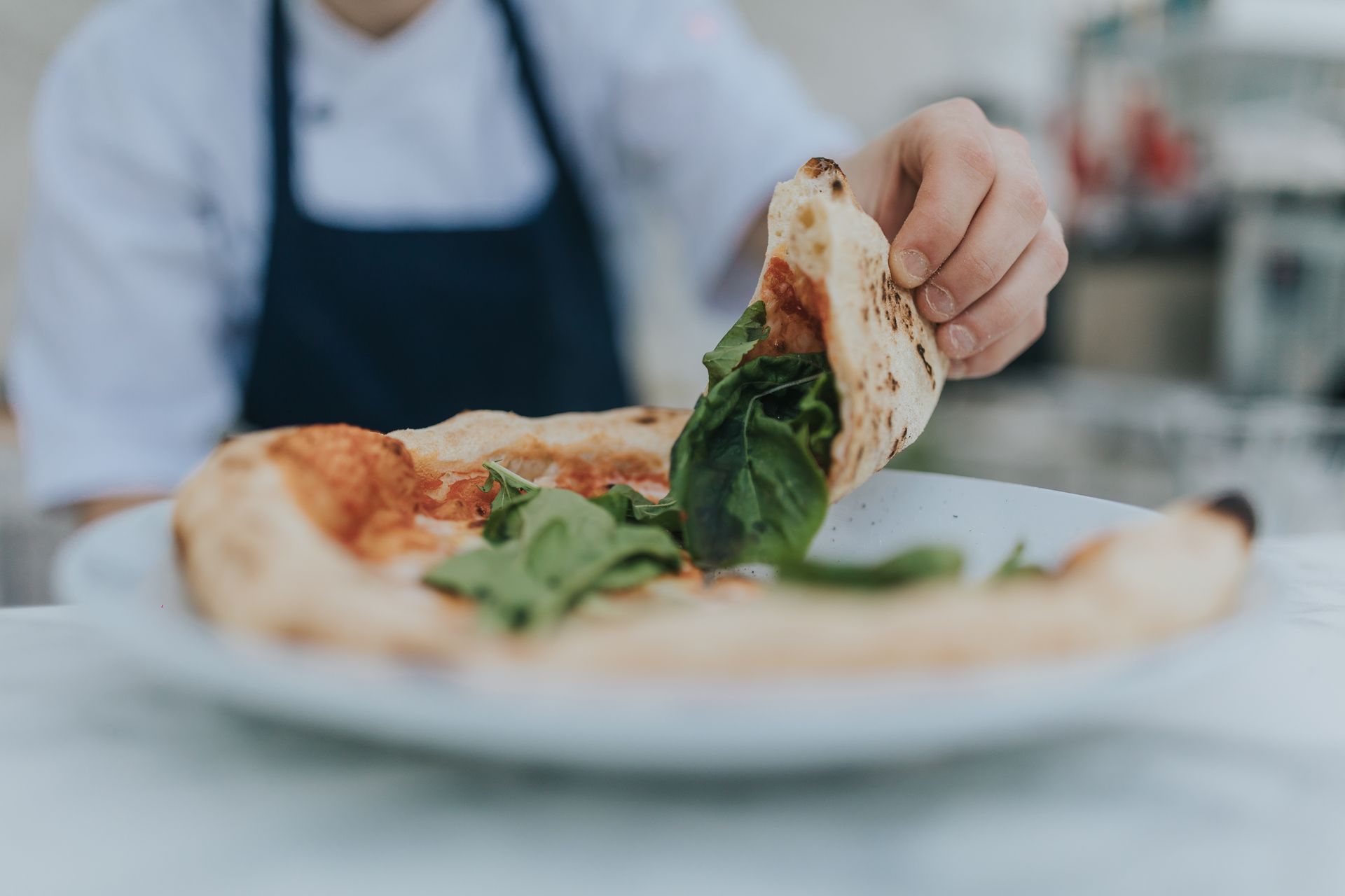 Chef holding a slice of pizza with basil, served on a white plate.