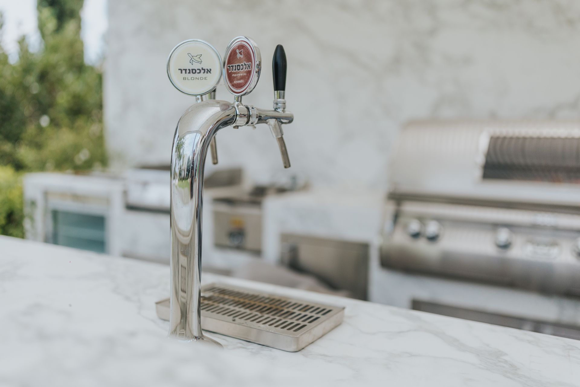 Chrome beer tap with two handles on a marble countertop, outdoor setting with a grill.