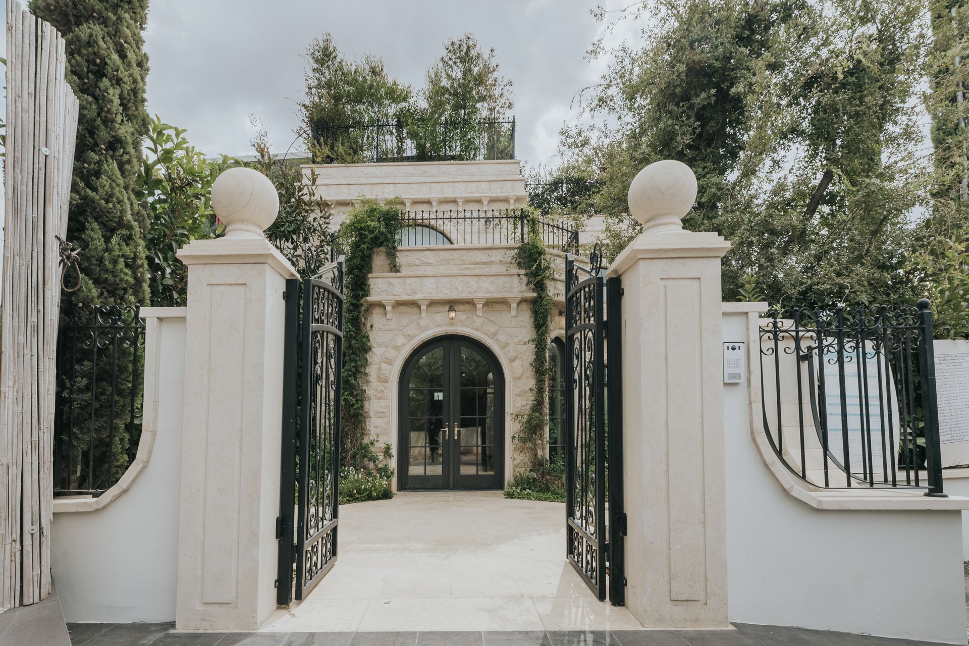 Stone building entrance with open black gates, archway, and a small rooftop garden.