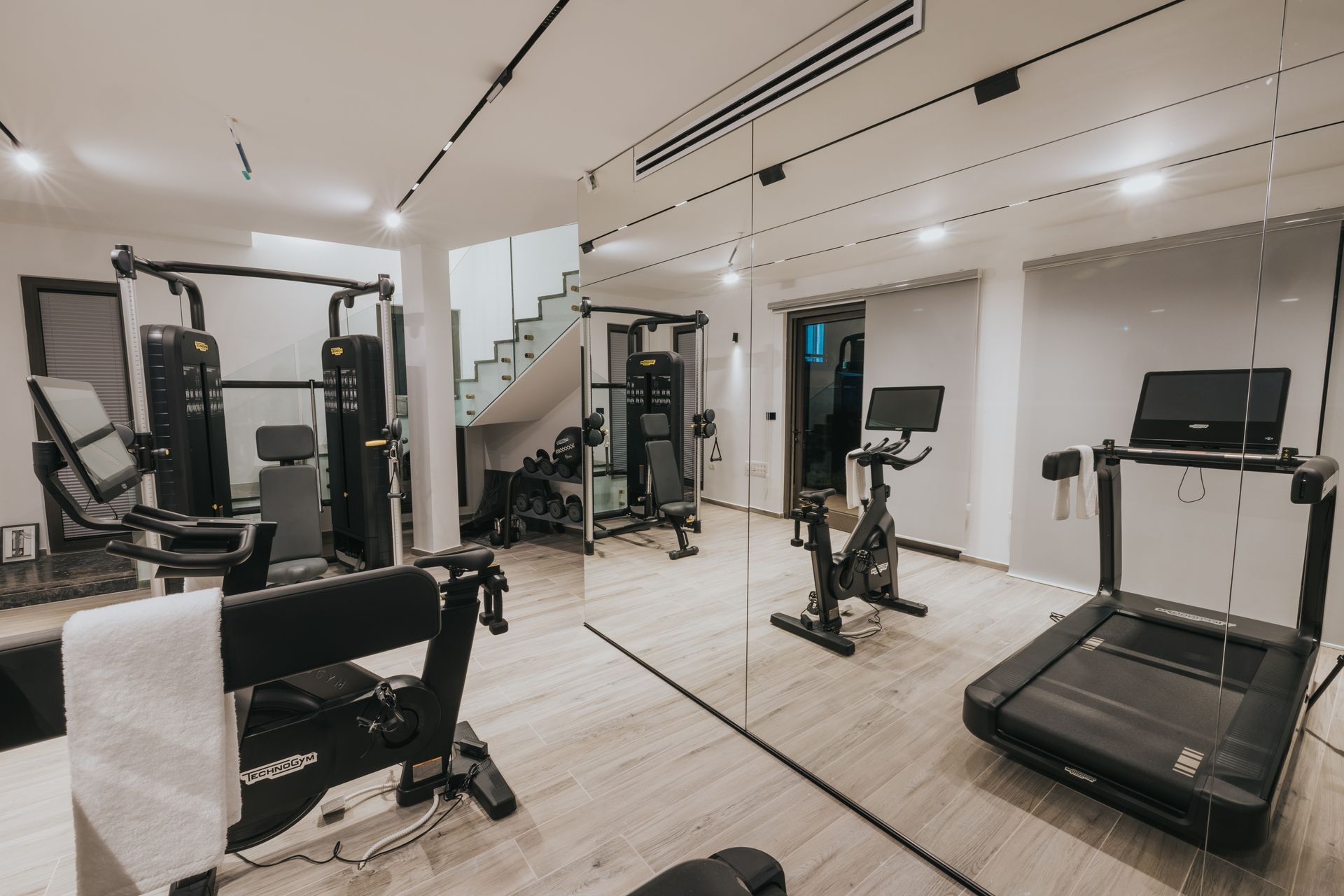 Home gym with exercise equipment: treadmill, stationary bike, weight machines, and a mirror.